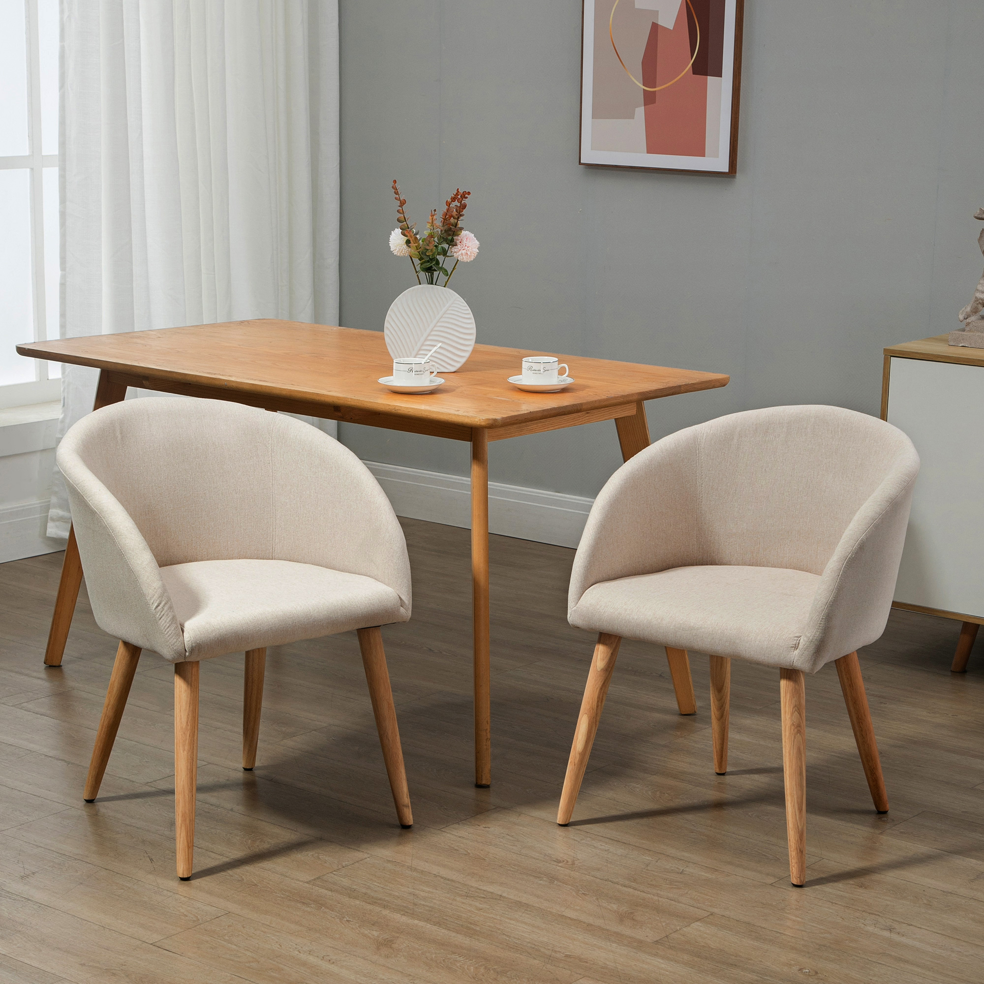 Due sedie imbottite beige di fronte a un tavolo di legno con fiori e tazze.