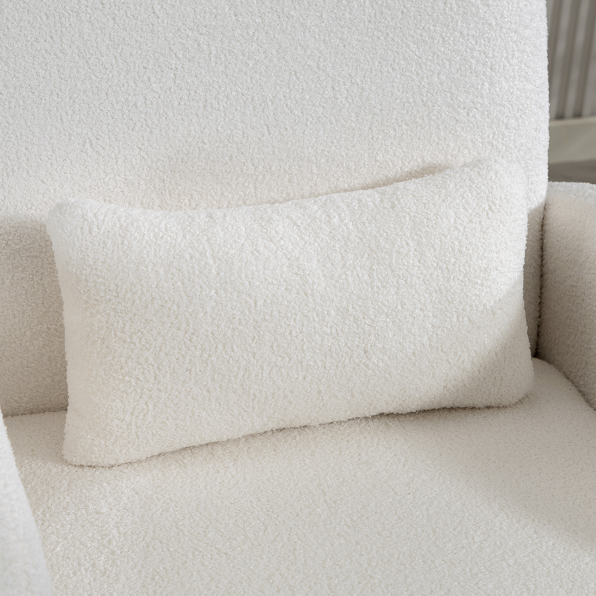 Un cuscino bianco in tessuto teddy riposa su una poltrona coordinata.