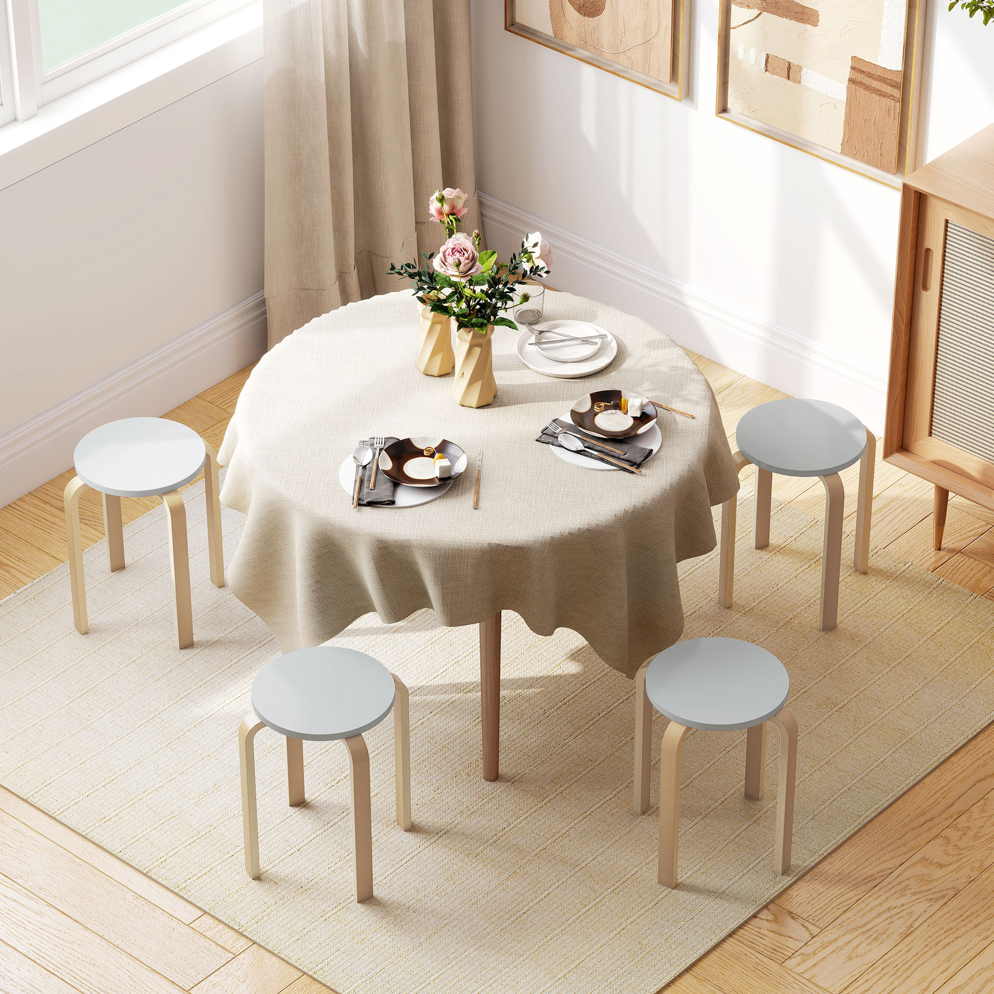Un tavolo rotondo con tovaglia beige chiaro, quattro sgabelli e fiori in vasi.
