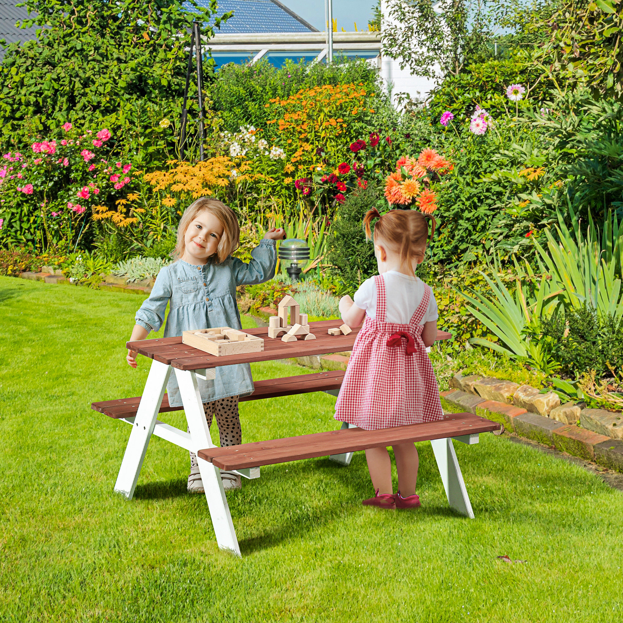 Due bambine giocano con blocchi di legno a un tavolo da picnic in un giardino fiorito.