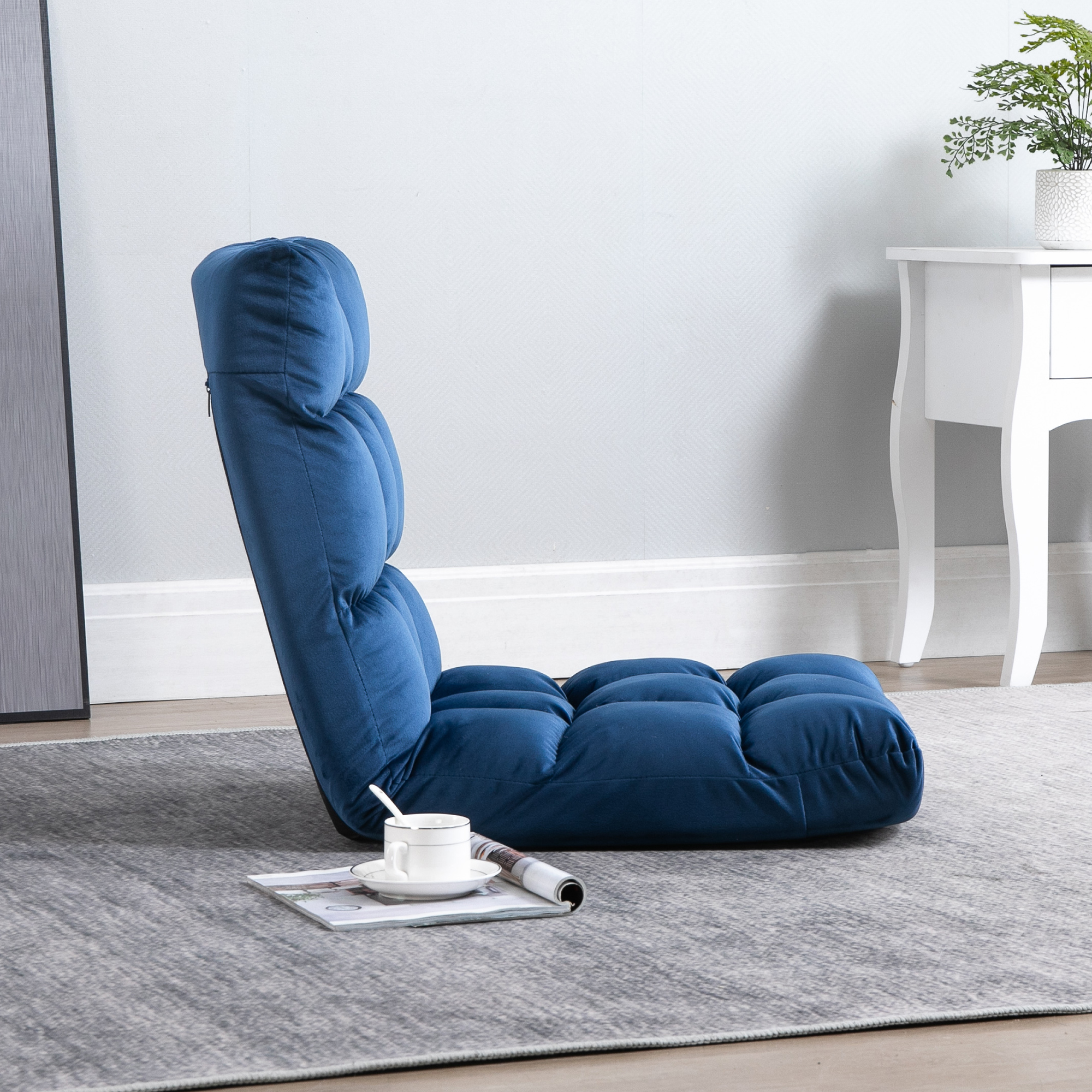 Una sedia da terra blu con cuscini giace su un tappeto grigio accanto a una tazza.