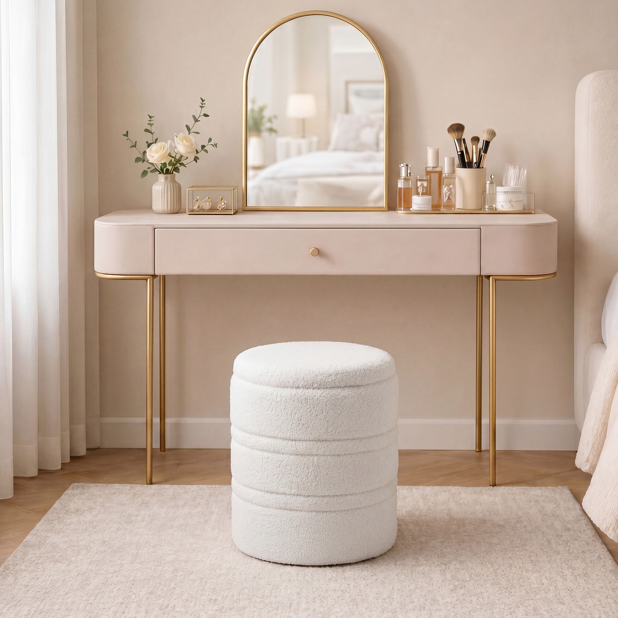 Una toeletta rosa pallido con gambe dorate e specchio. Un pouf bianco davanti.