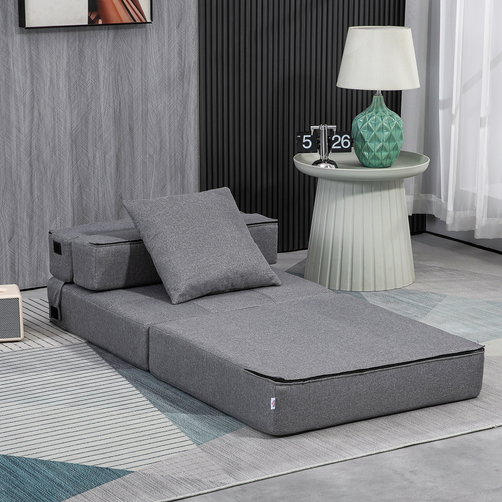 Un divano letto grigio con cuscino e lampada su un tavolino.