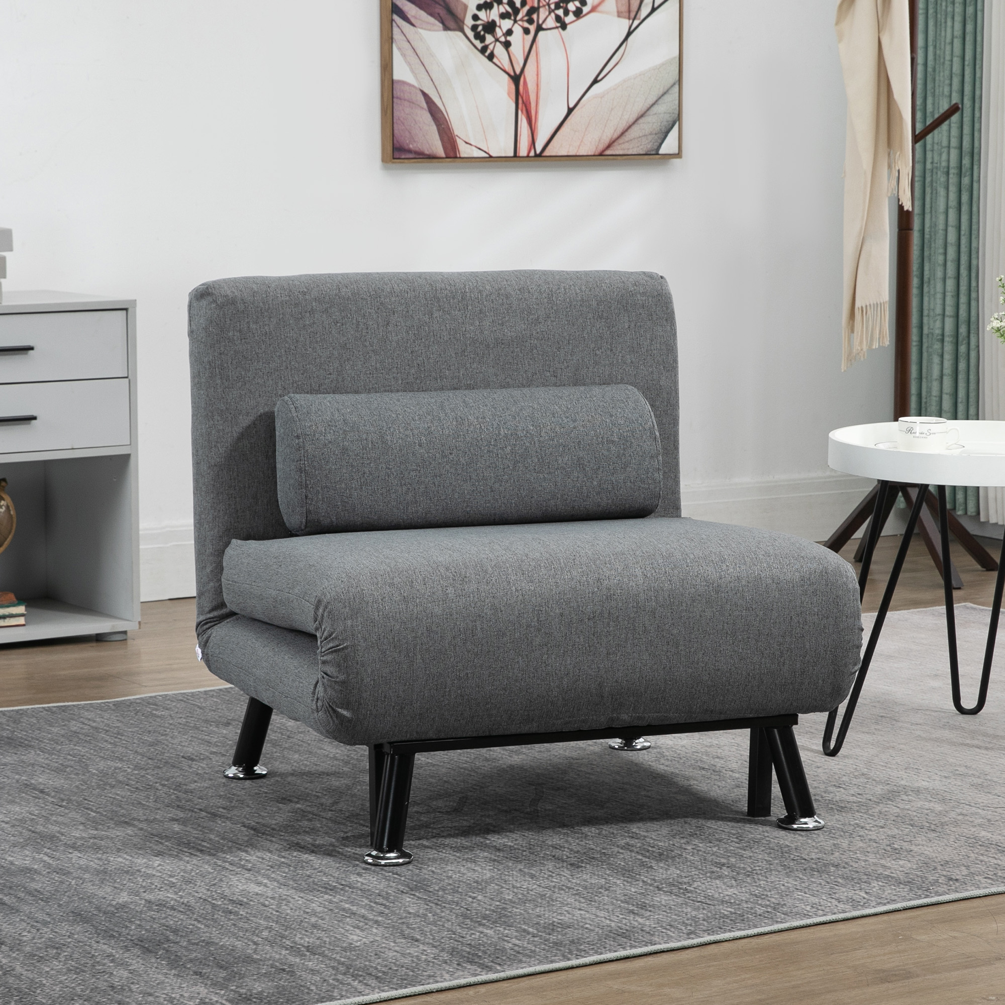 Divano letto grigio con cuscino schienale, su tappeto grigio, vicino a tavolino.