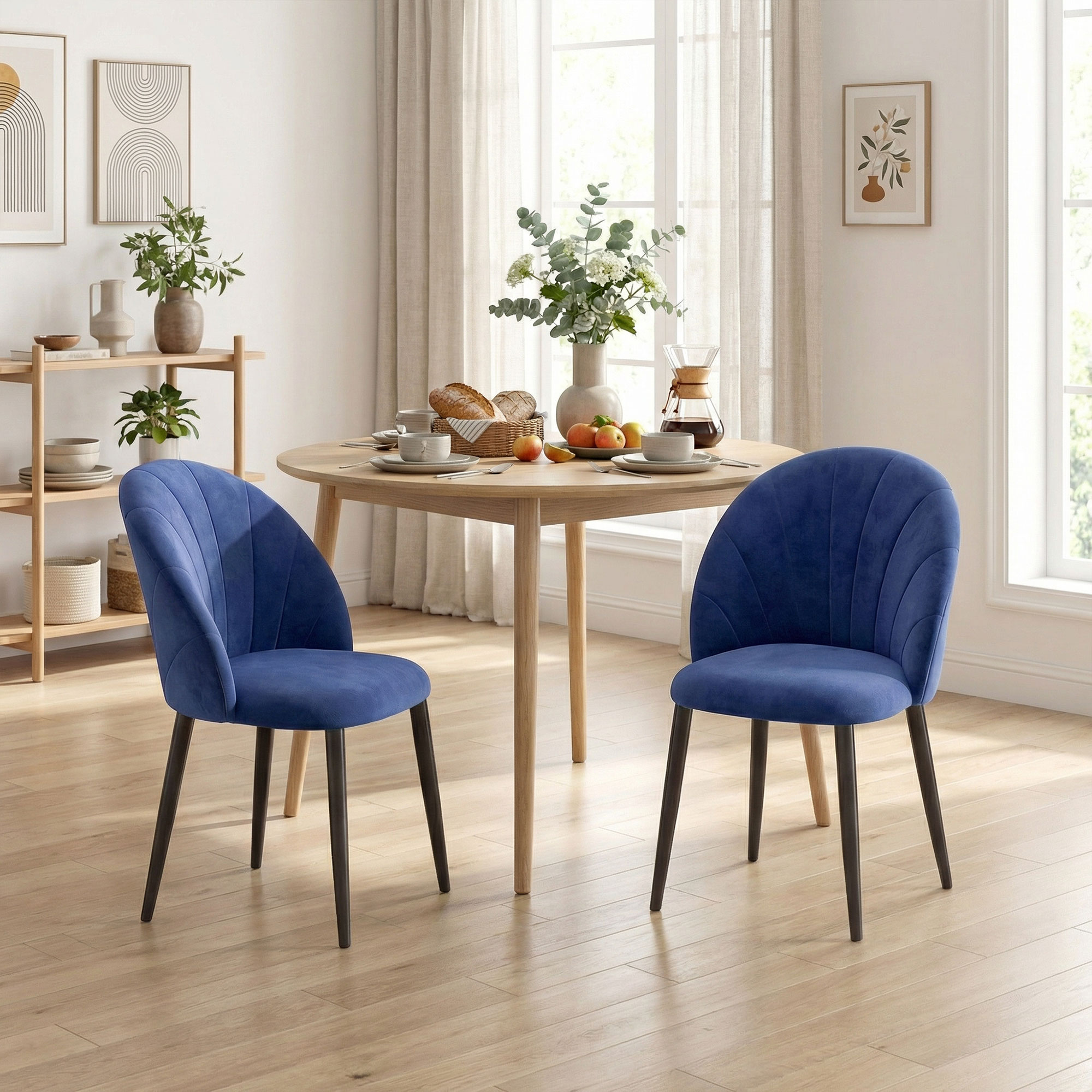 Due sedie blu di velluto fiancheggiano un tavolo rotondo in legno con articoli per la colazione.