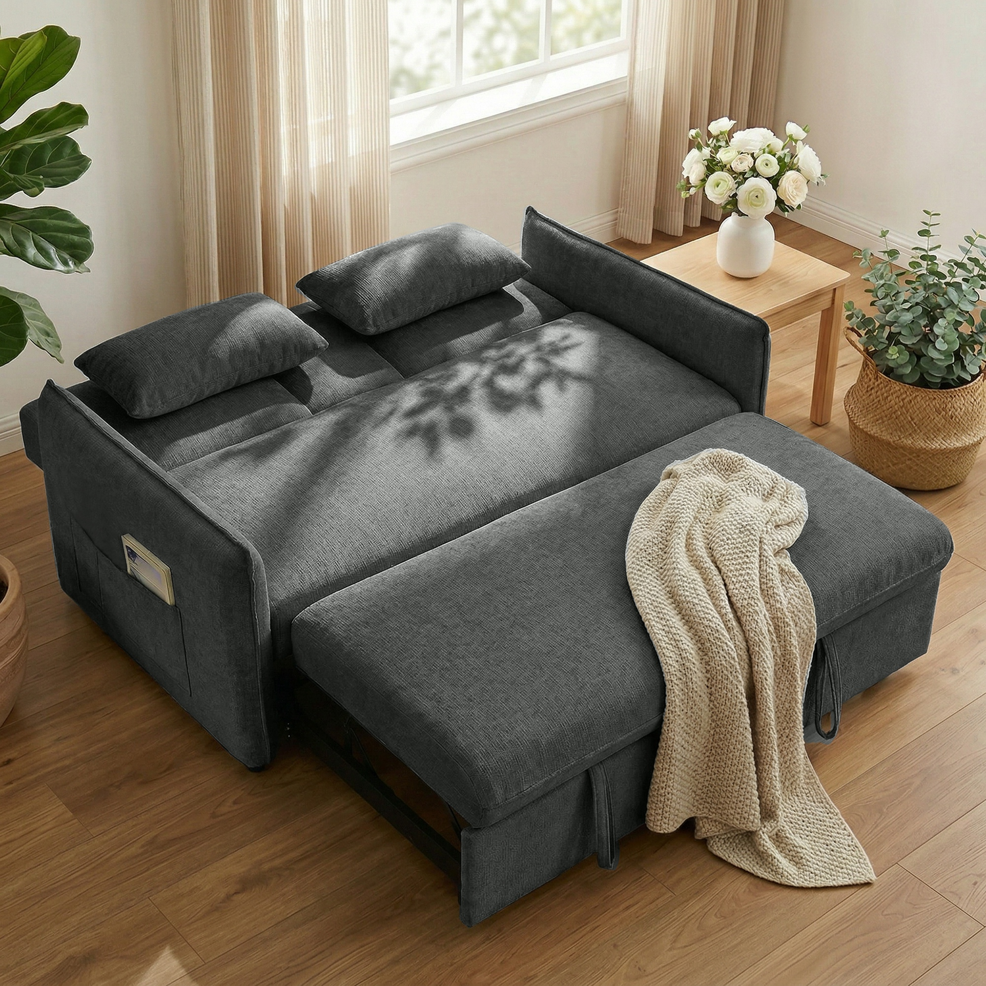 Un divano letto grigio con cuscini e coperta, vicino a un tavolo di legno con fiori.