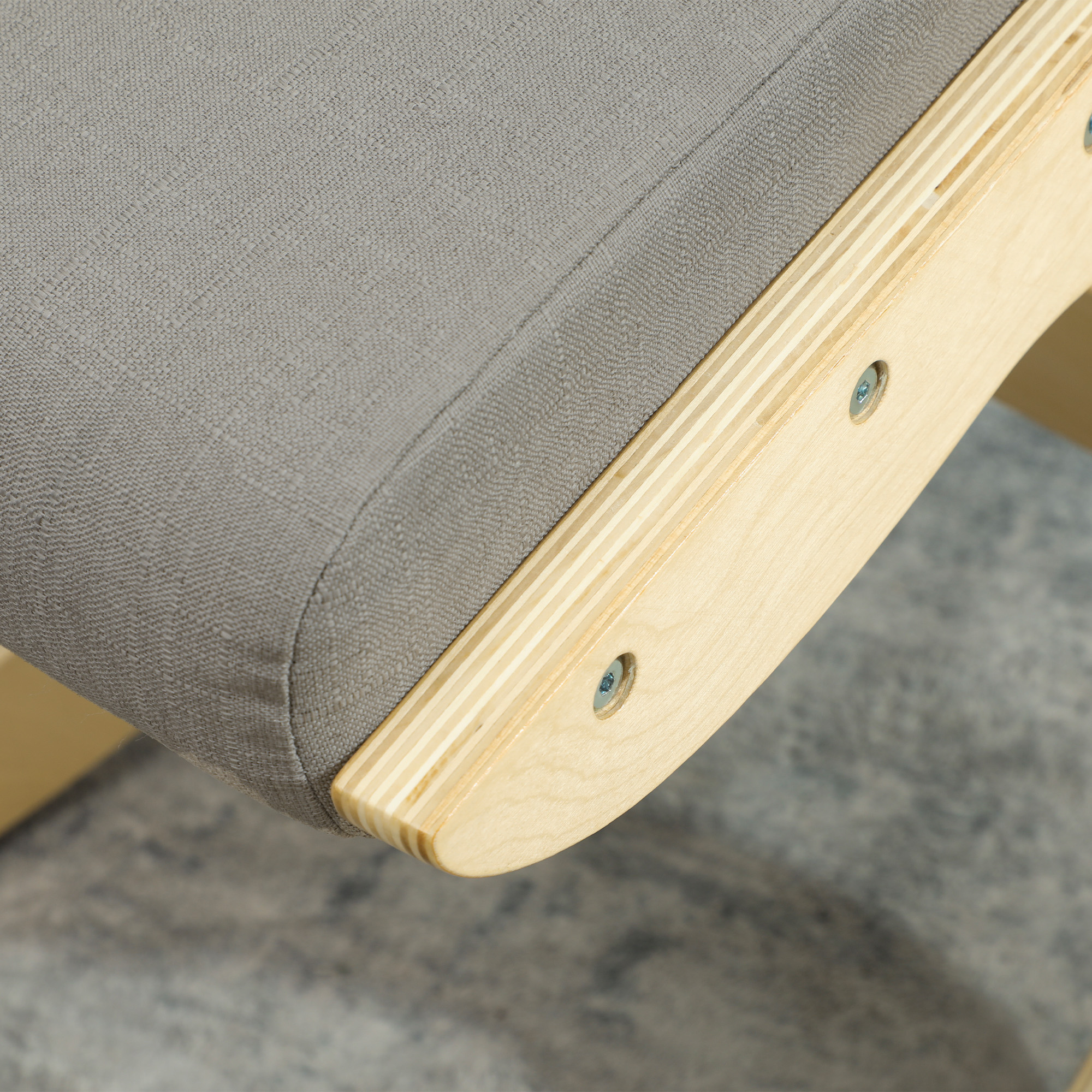 Primo piano di un cuscino in tessuto grigio su una cornice in legno curva con viti a vista.