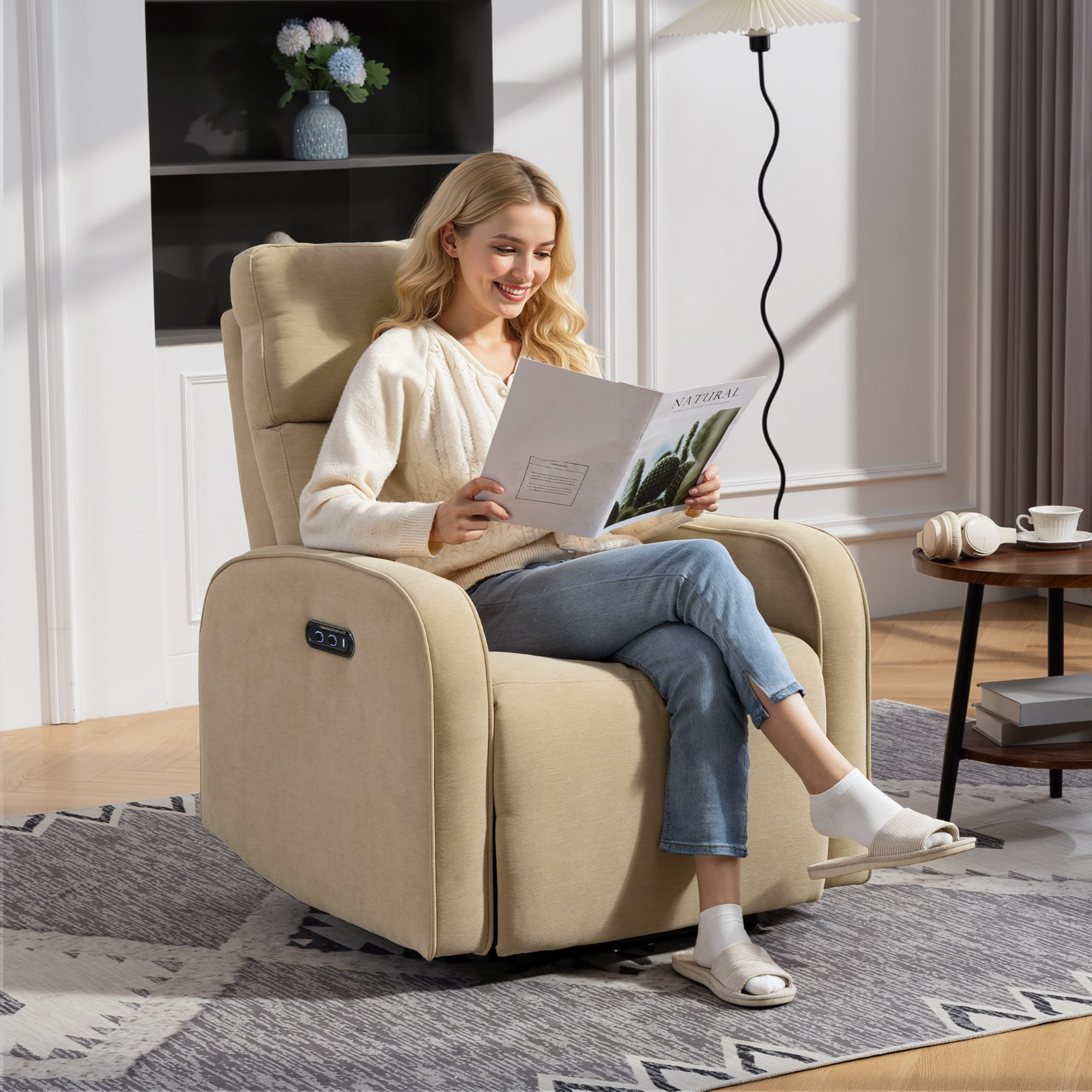Una donna legge una rivista seduta su una poltrona reclinabile beige. Indossa jeans.