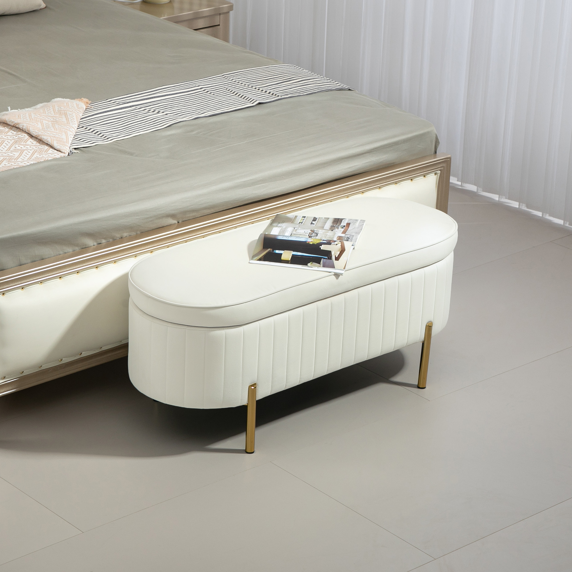 Una poltrona-pouf bianca imbottita con gambe dorate davanti a un letto.