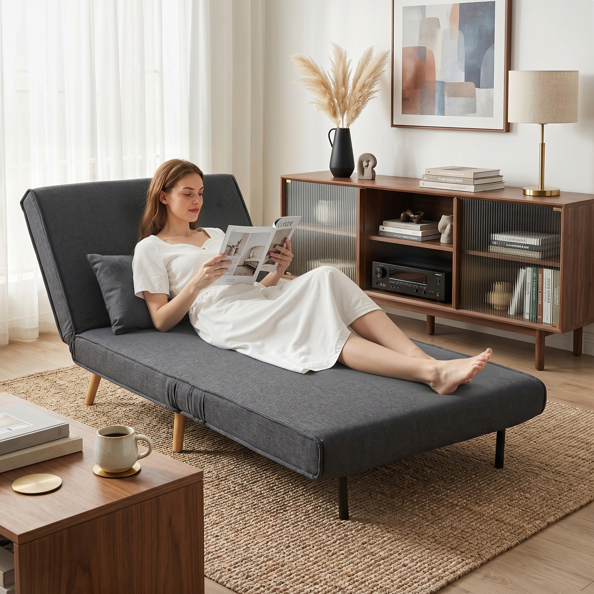 Una donna legge una rivista rilassandosi su un divano letto grigio.