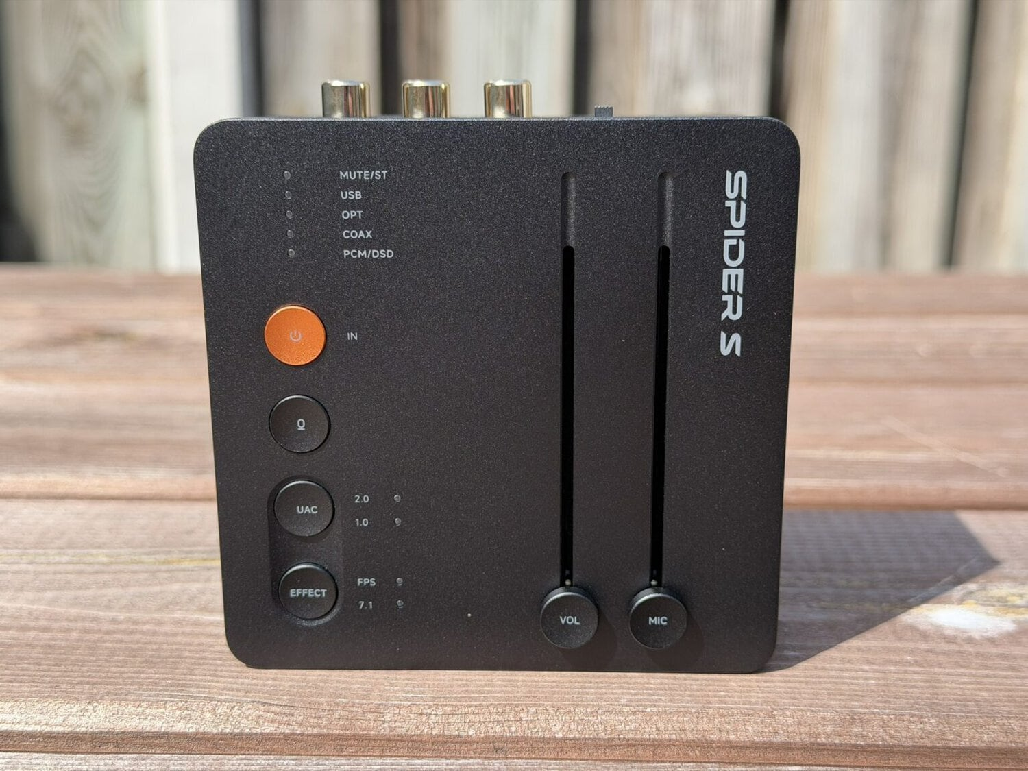 Dispositivo audio nero etichettato SPIDERS con pulsanti e slider su una superficie di legno.