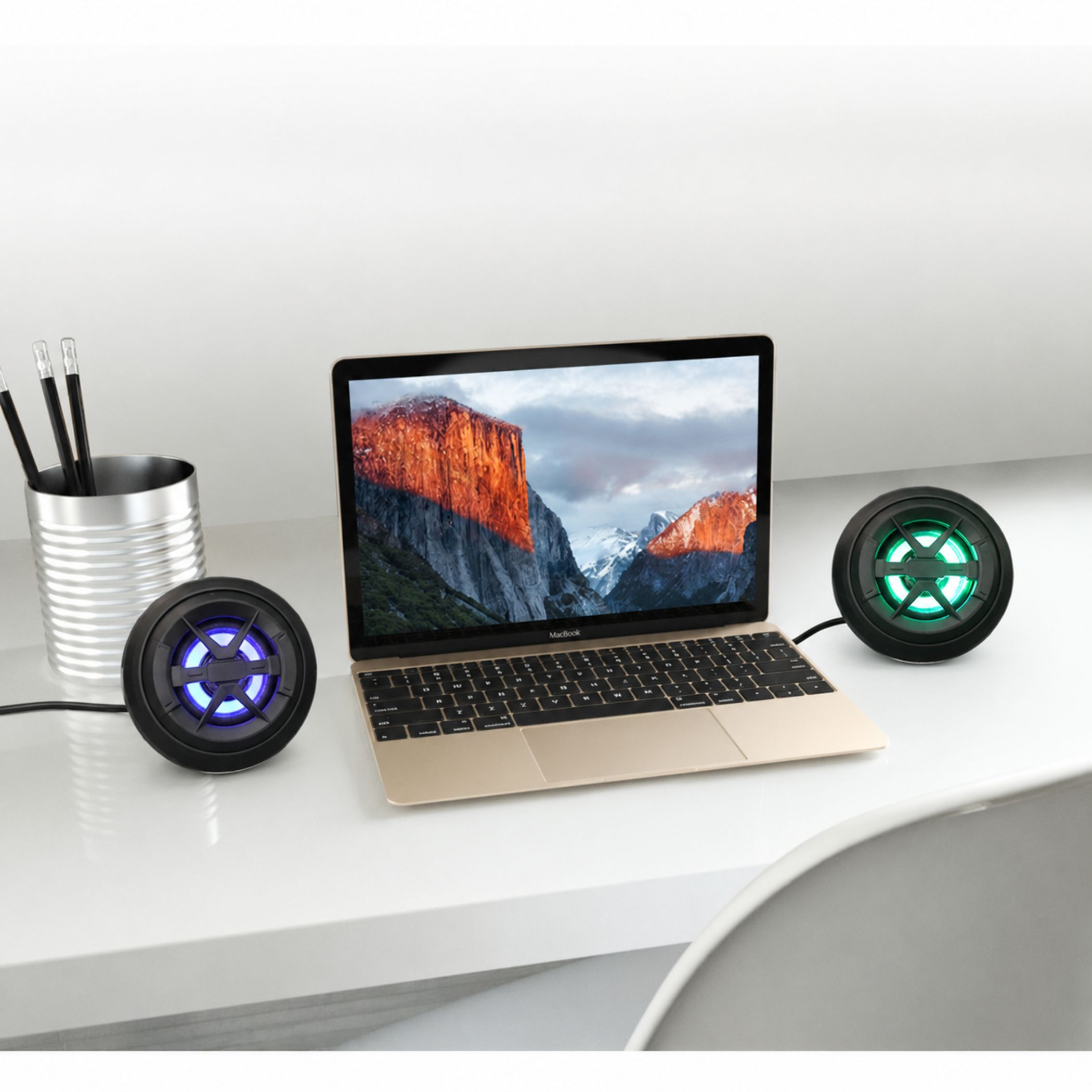 Ein Laptop steht auf einem Schreibtisch mit zwei leuchtenden Lautsprechern daneben.