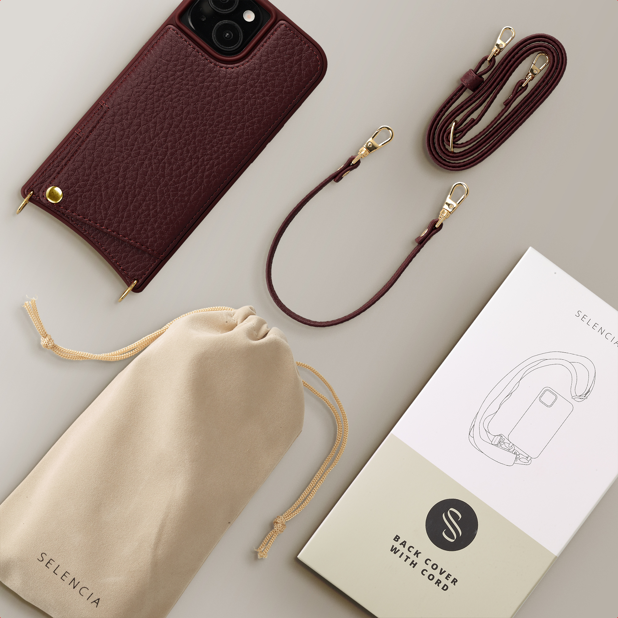 A burgundy phone case with straps and a drawstring pouch are laid out on a gray surface.