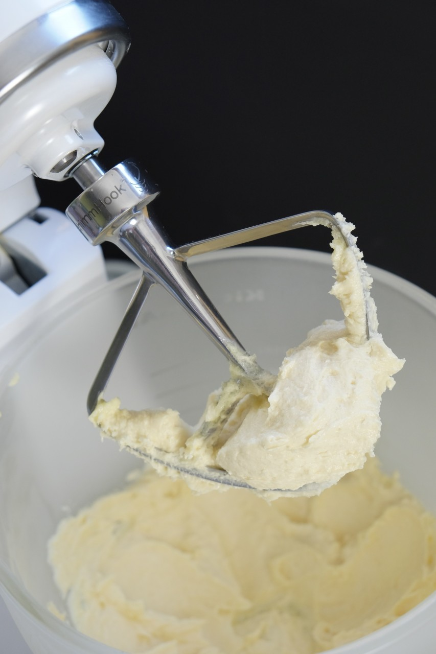Ein weißer Standmixer mit einem metallischen Rührbesen, der cremigen Teig aufnimmt.