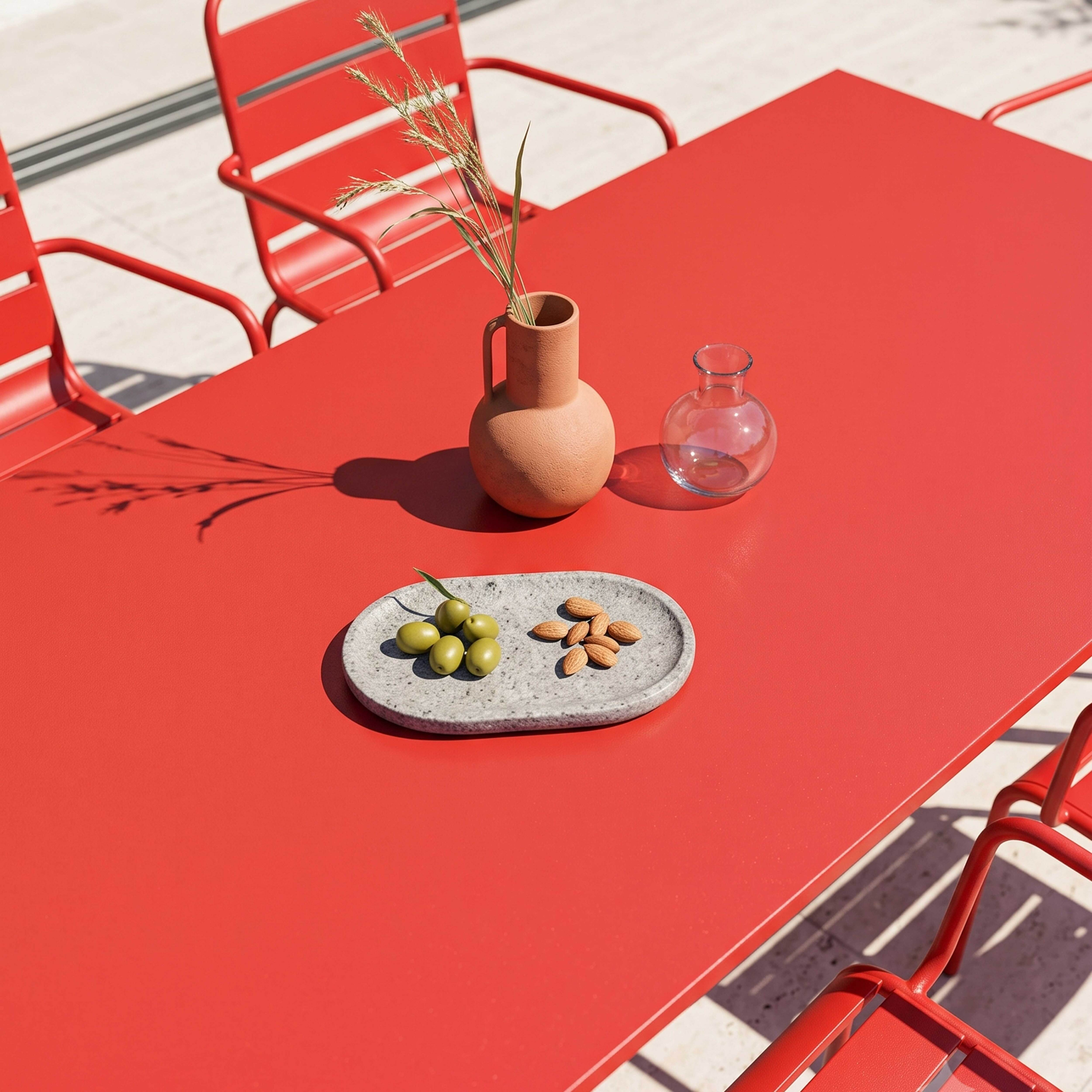 Roter Tisch mit Terracotta-Vase, Glasvase, Oliven und Mandeln.