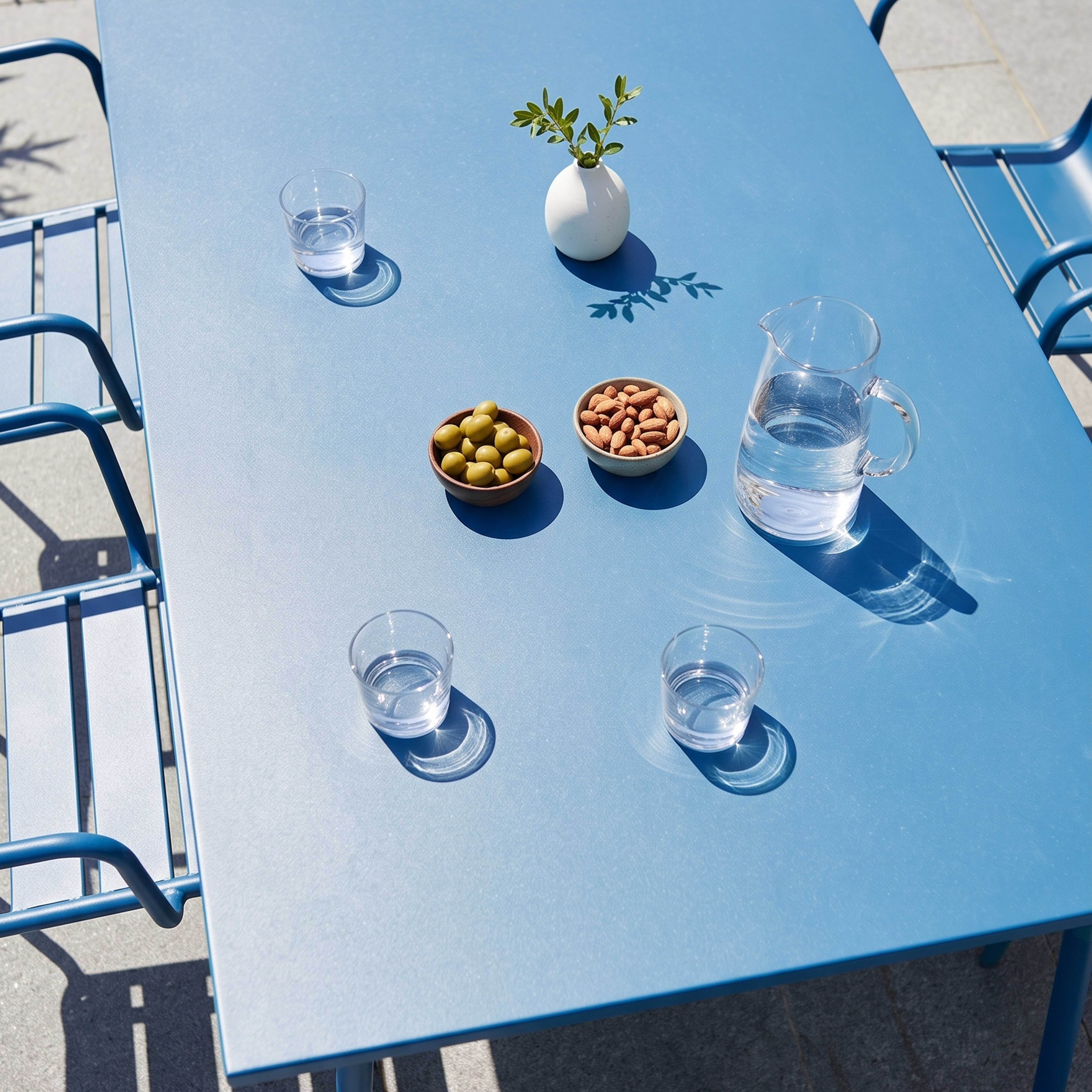 Blauer Tisch mit Wassergläsern, Oliven, Nüssen, einer Vase und einem Krug Wasser.