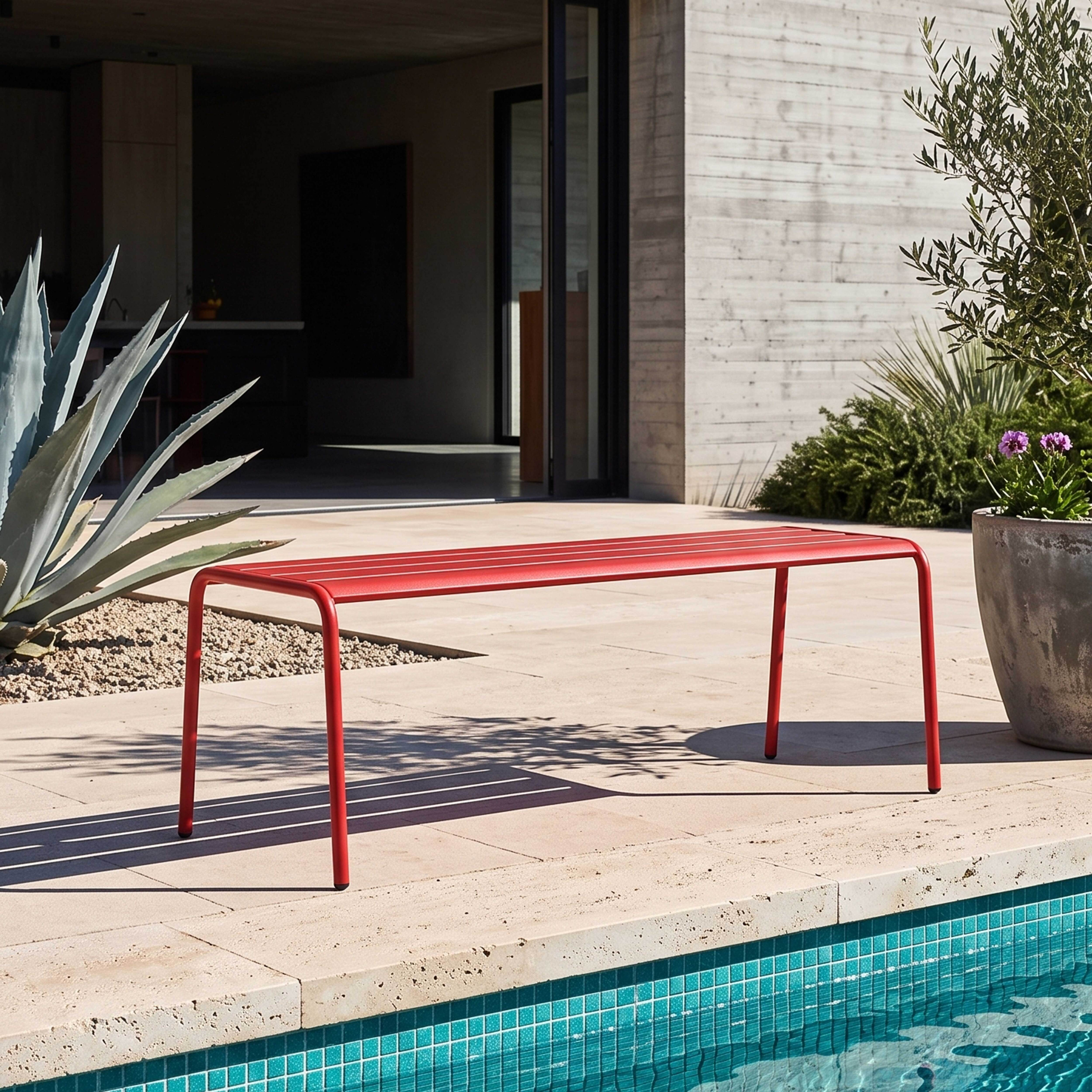 Rote Bank am Poolrand mit Betonwand und Pflanzen.