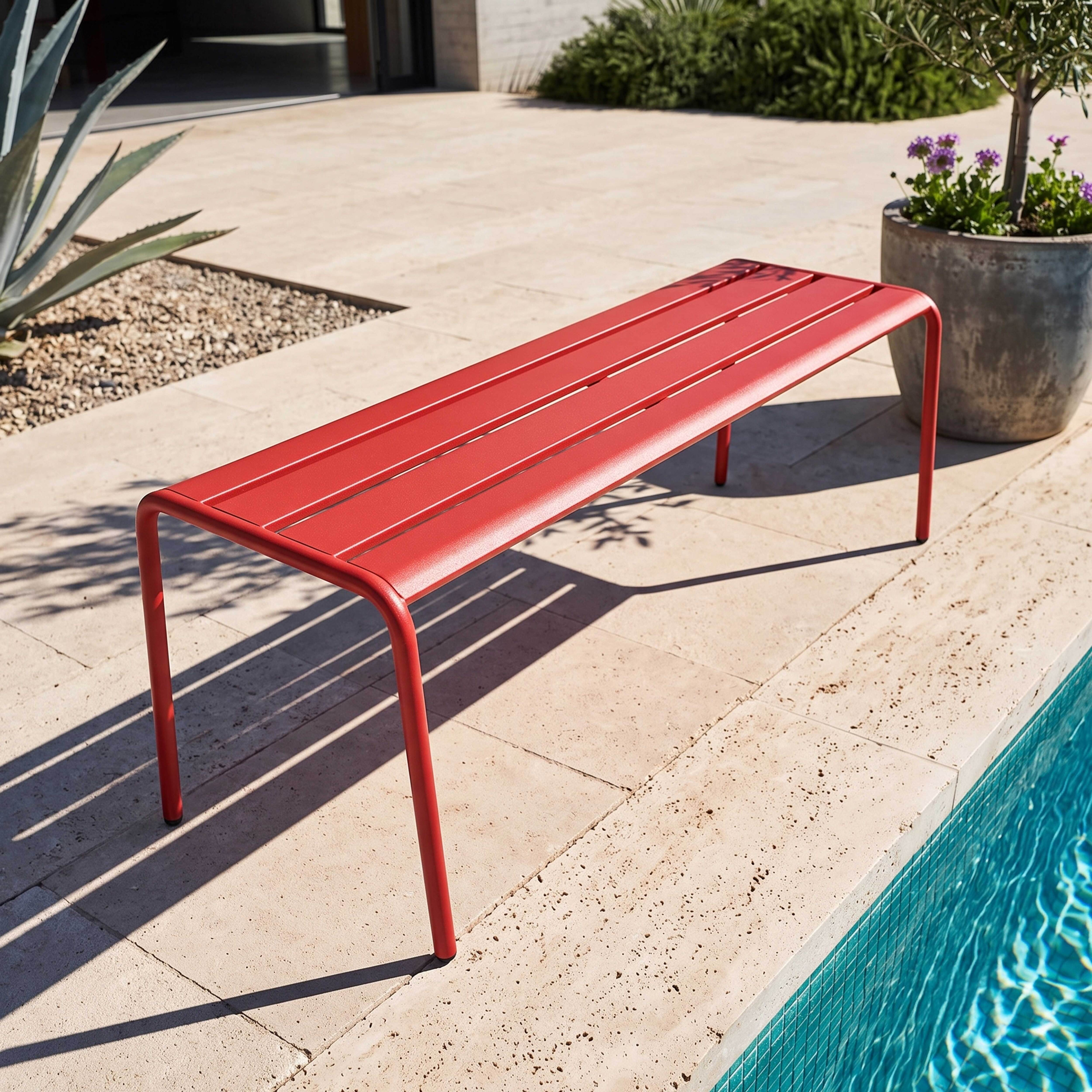 Eine rote Metallbank steht auf einer Travertin-Terrasse neben einem türkisfarbenen Pool.