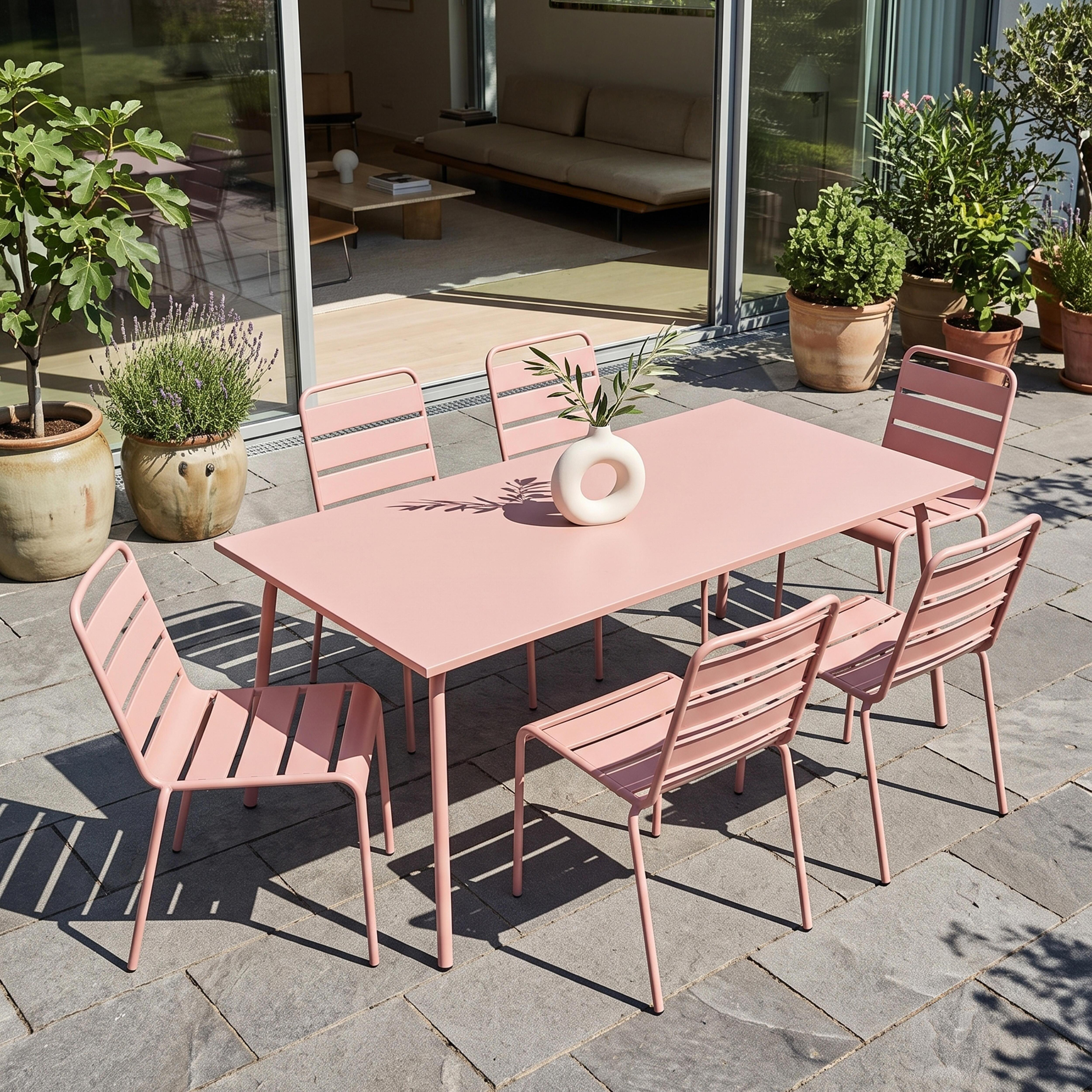 Ein rosafarbener Gartentisch mit Stühlen auf einer Steinterrasse, daneben Pflanzen.