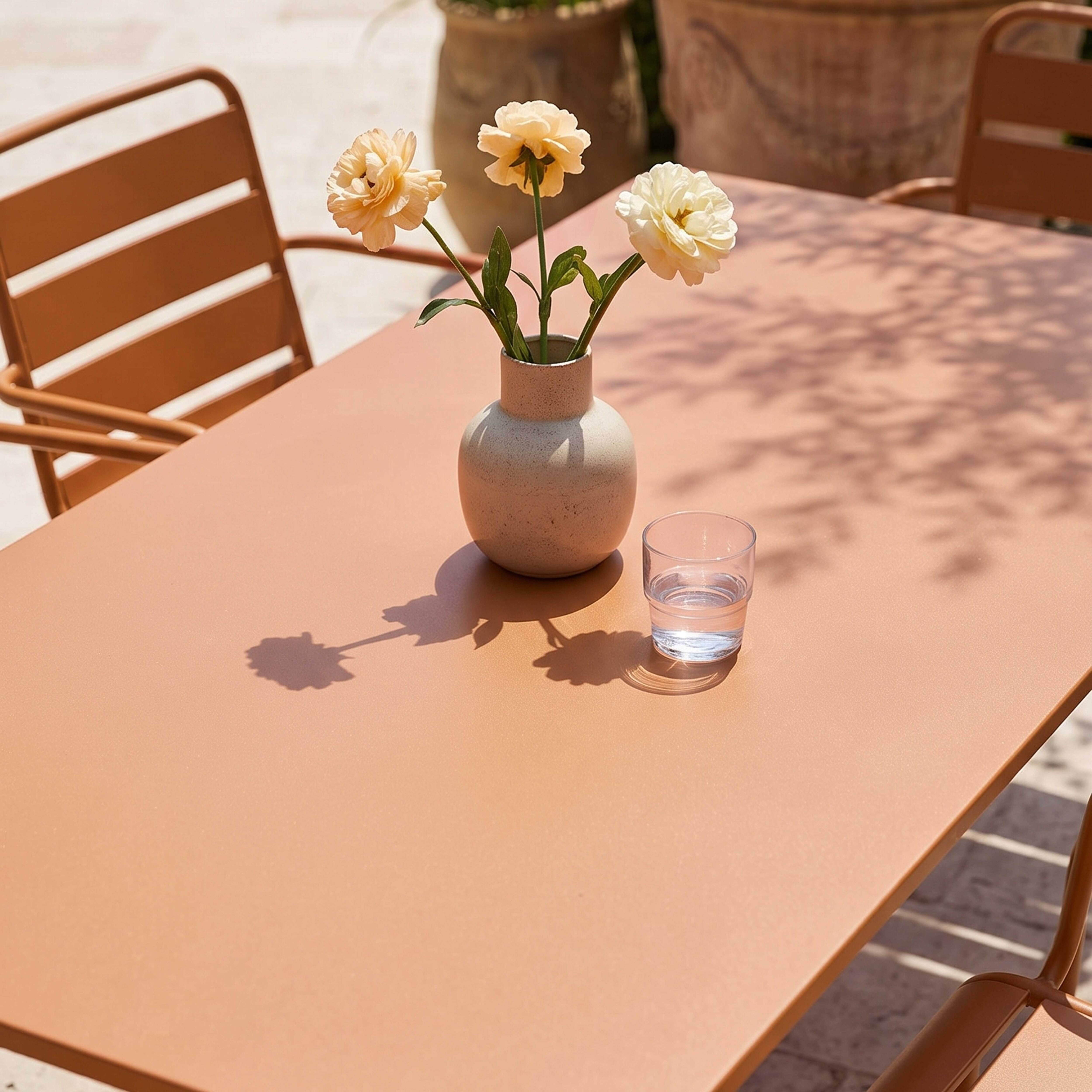Ein Tisch mit Blumen und einem Glas Wasser, daneben braune Stühle.