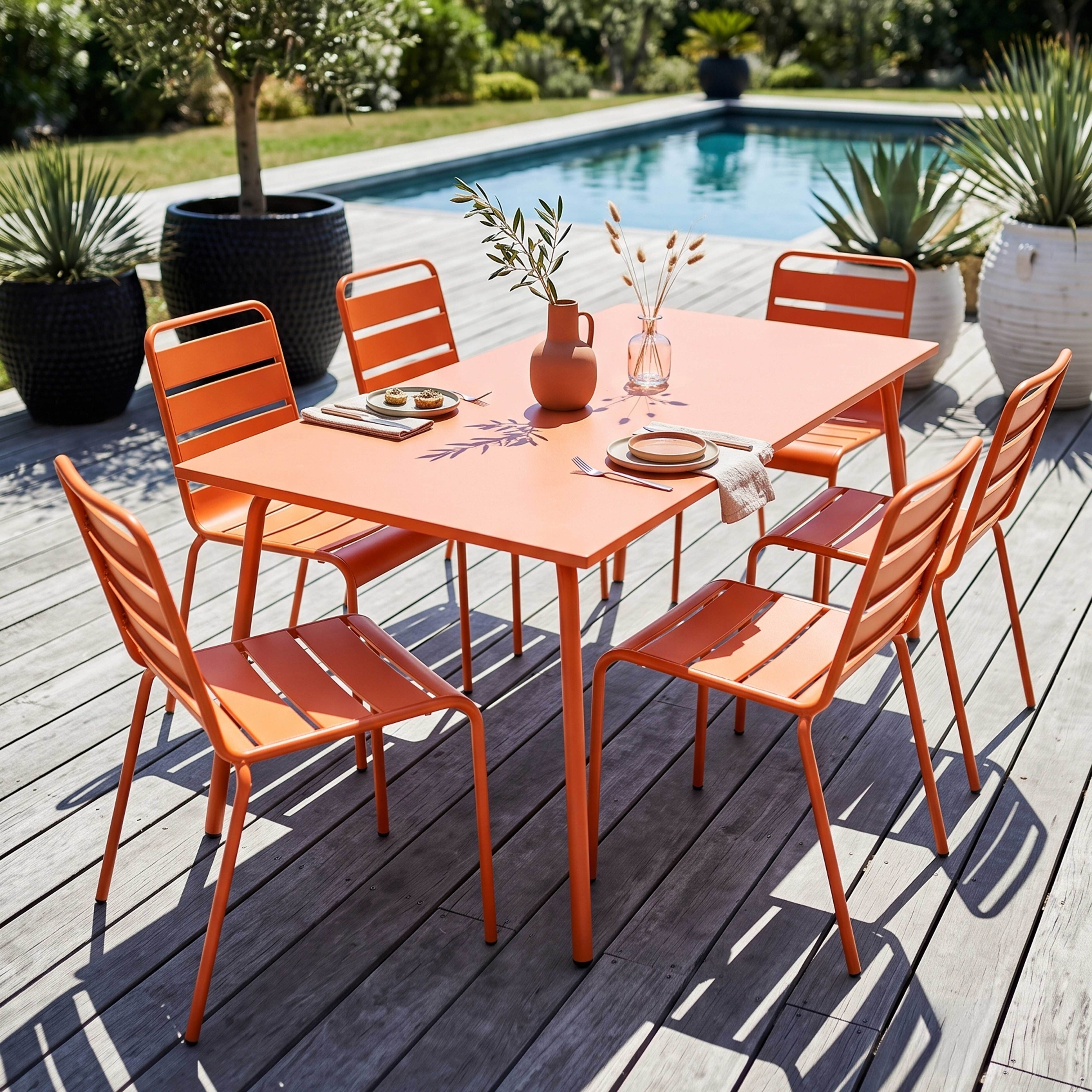 Ein orangefarner Tisch und Stühle stehen auf einer Holzterrasse neben einem Pool.