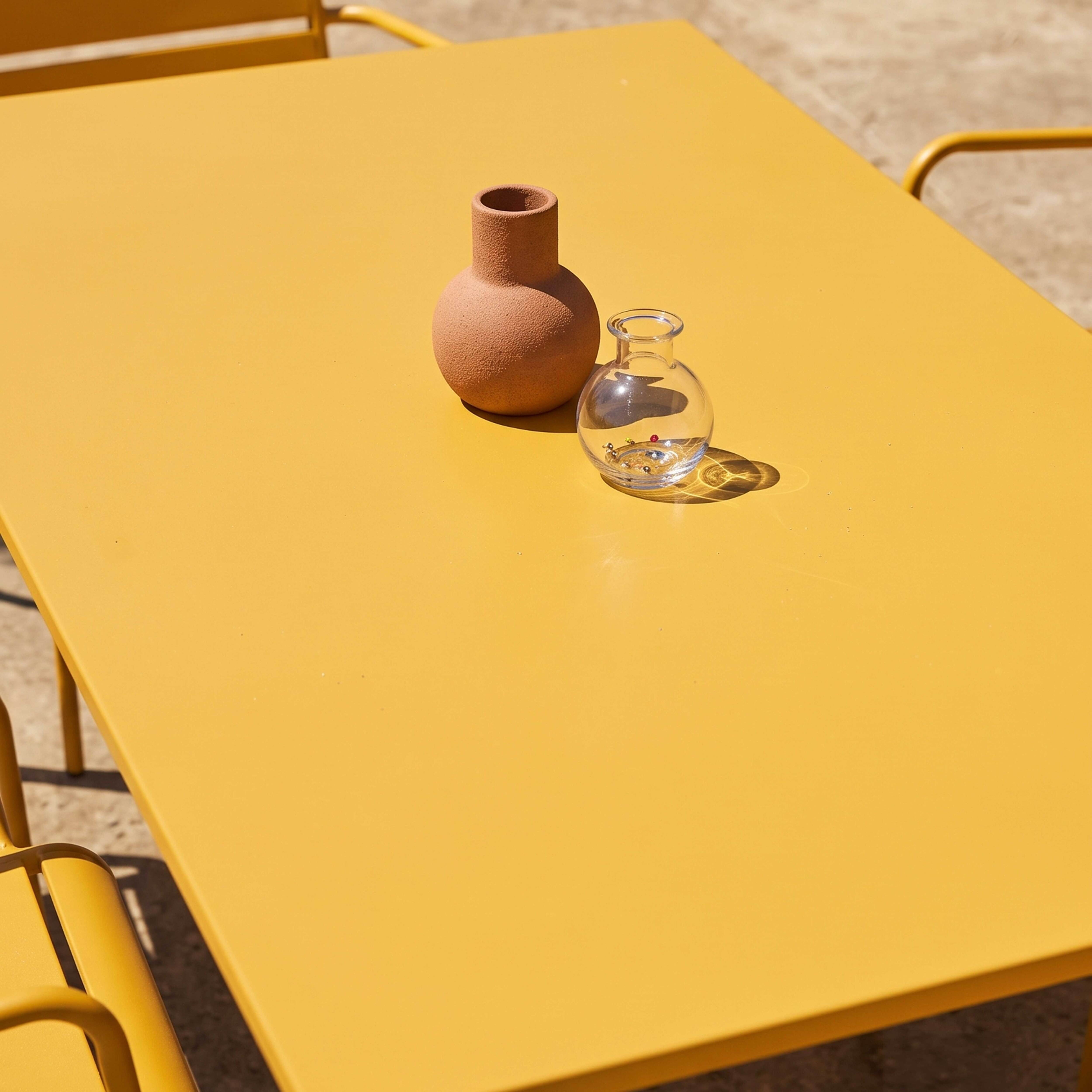 Eine runde Terrakotta-Vase und eine kleine Glasvase mit Kugeln auf einem gelben Tisch.