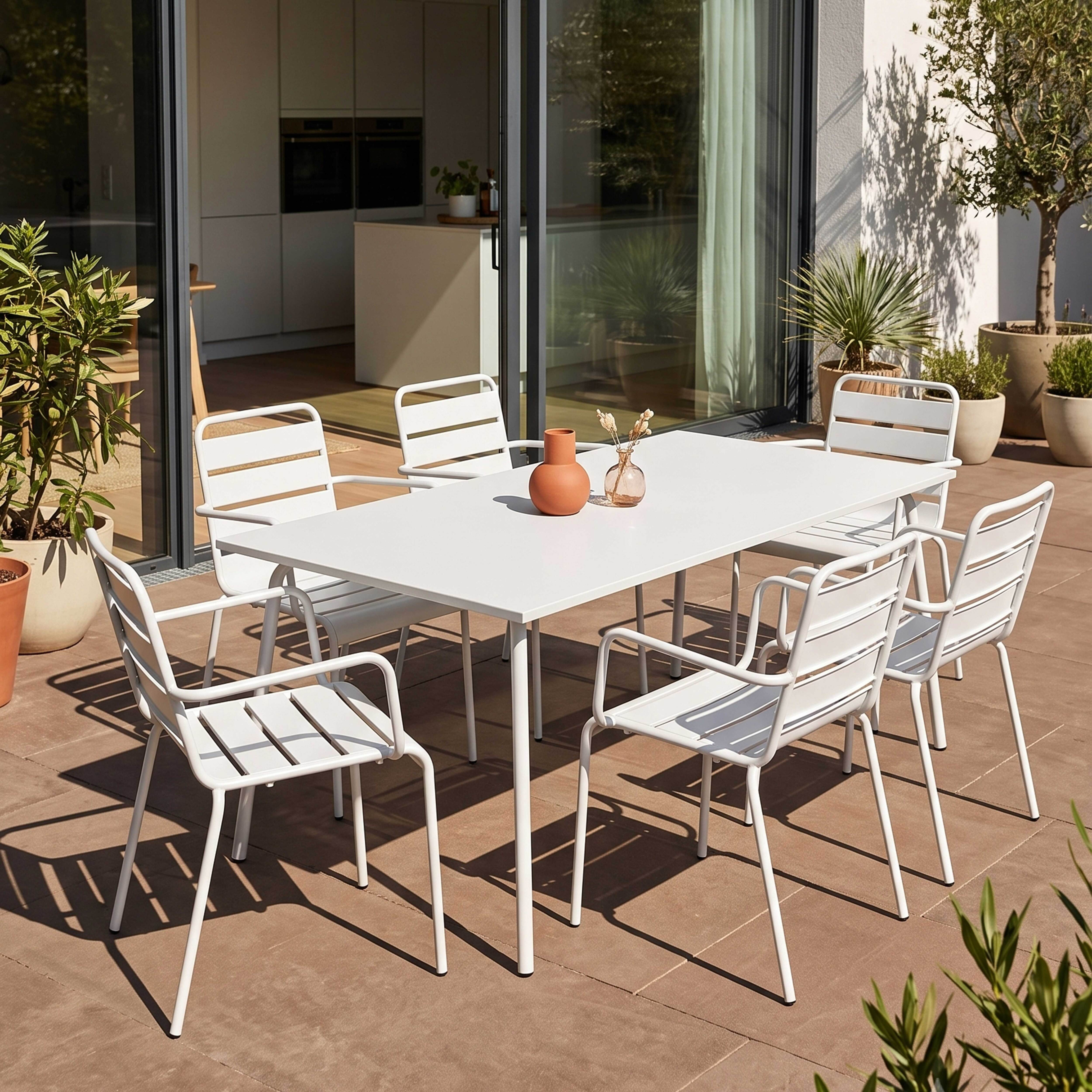 Weier Esstisch mit Stöhlen auf einer Terrasse mit Pflanzen und Schatten.