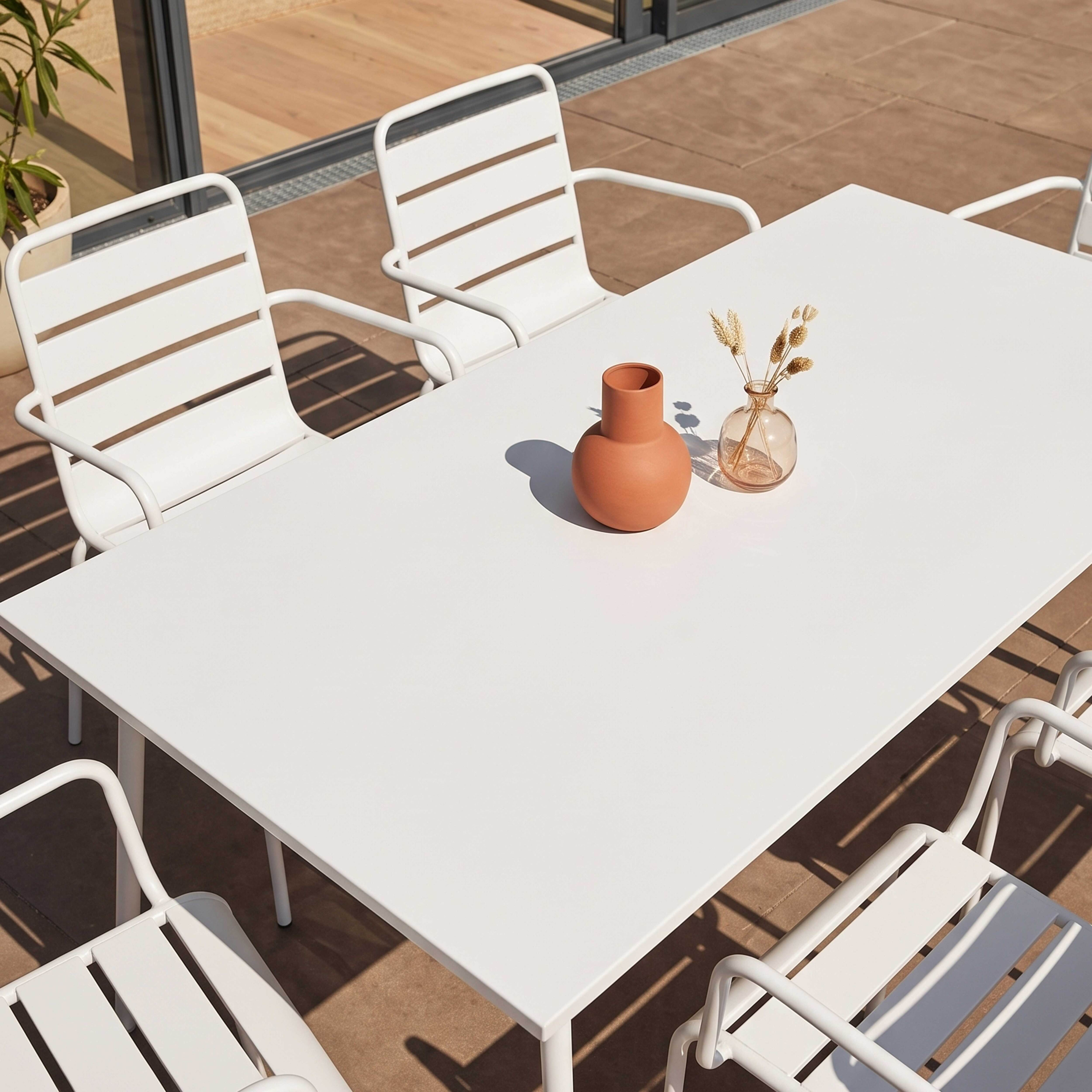 Weiße Gartenmöbel mit Vasen auf einem Tisch und Holzboden.