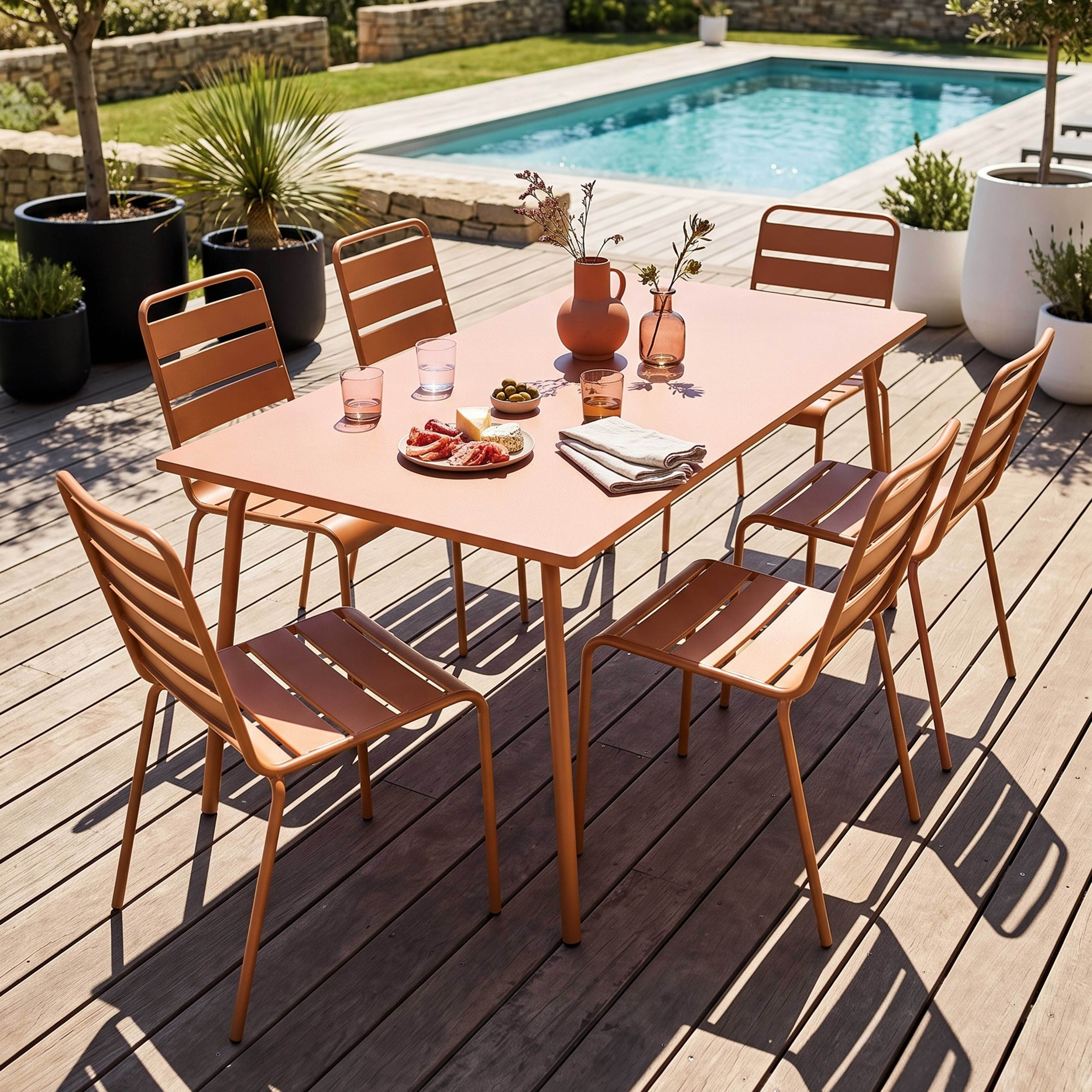 Ein rosafarbener Tisch mit Stühlen auf einer Holzterrasse, daneben ein Pool.