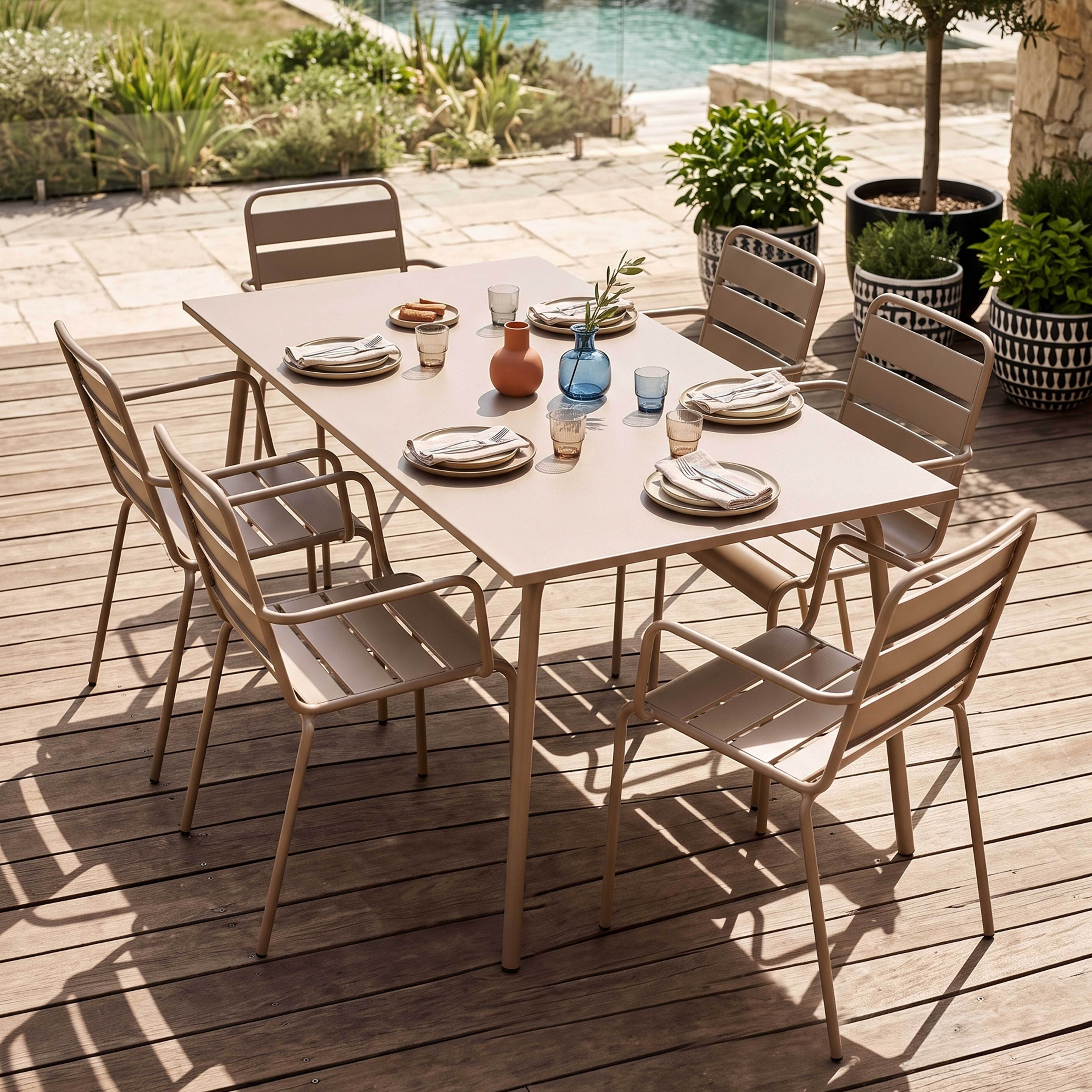 Ein Esstisch mit Stühlen auf einer Holzterrasse mit Pool und Pflanzen im Hintergrund.