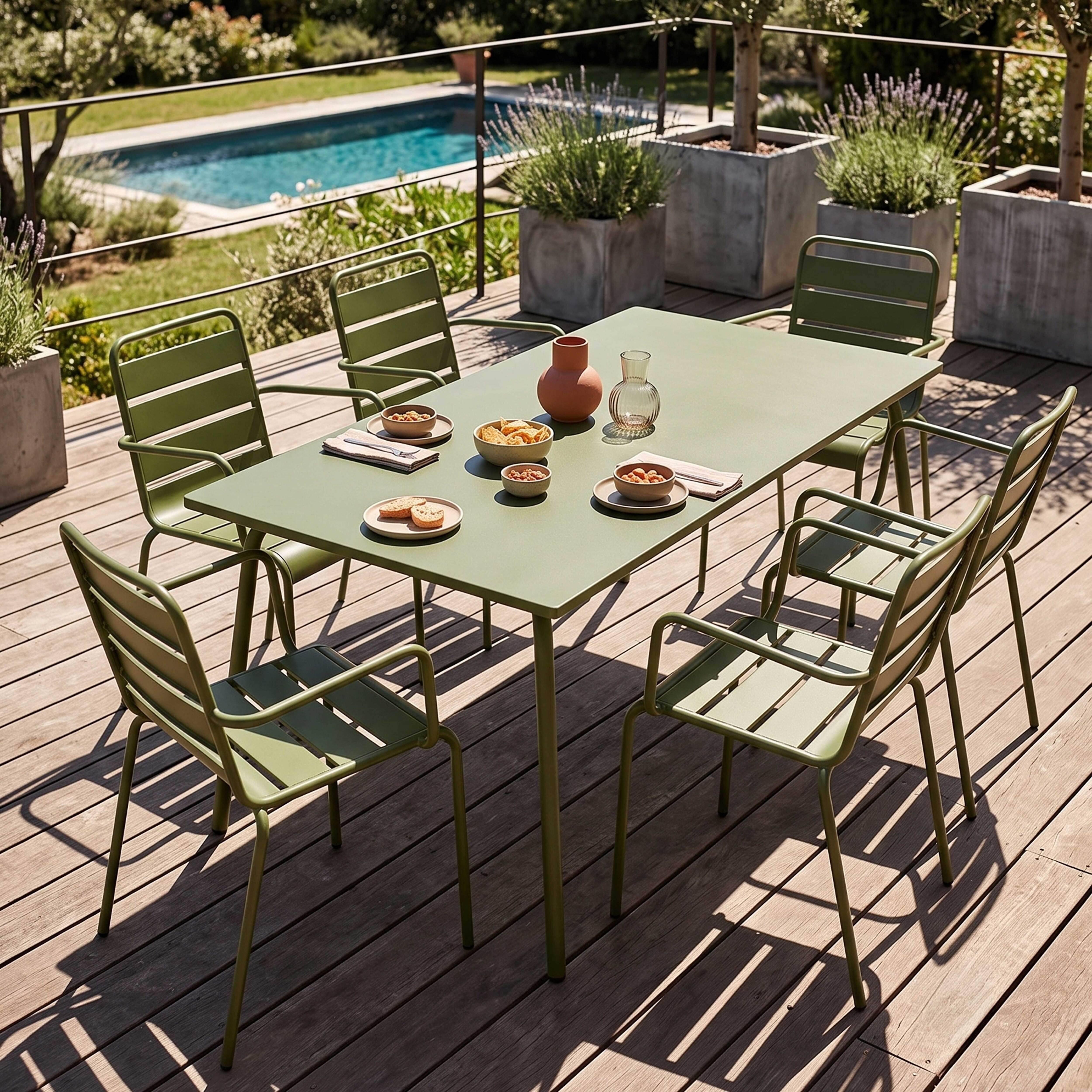 Ein grüner Gartentisch mit Stühlen steht auf einer Holzterrasse, Pool im Hintergrund.