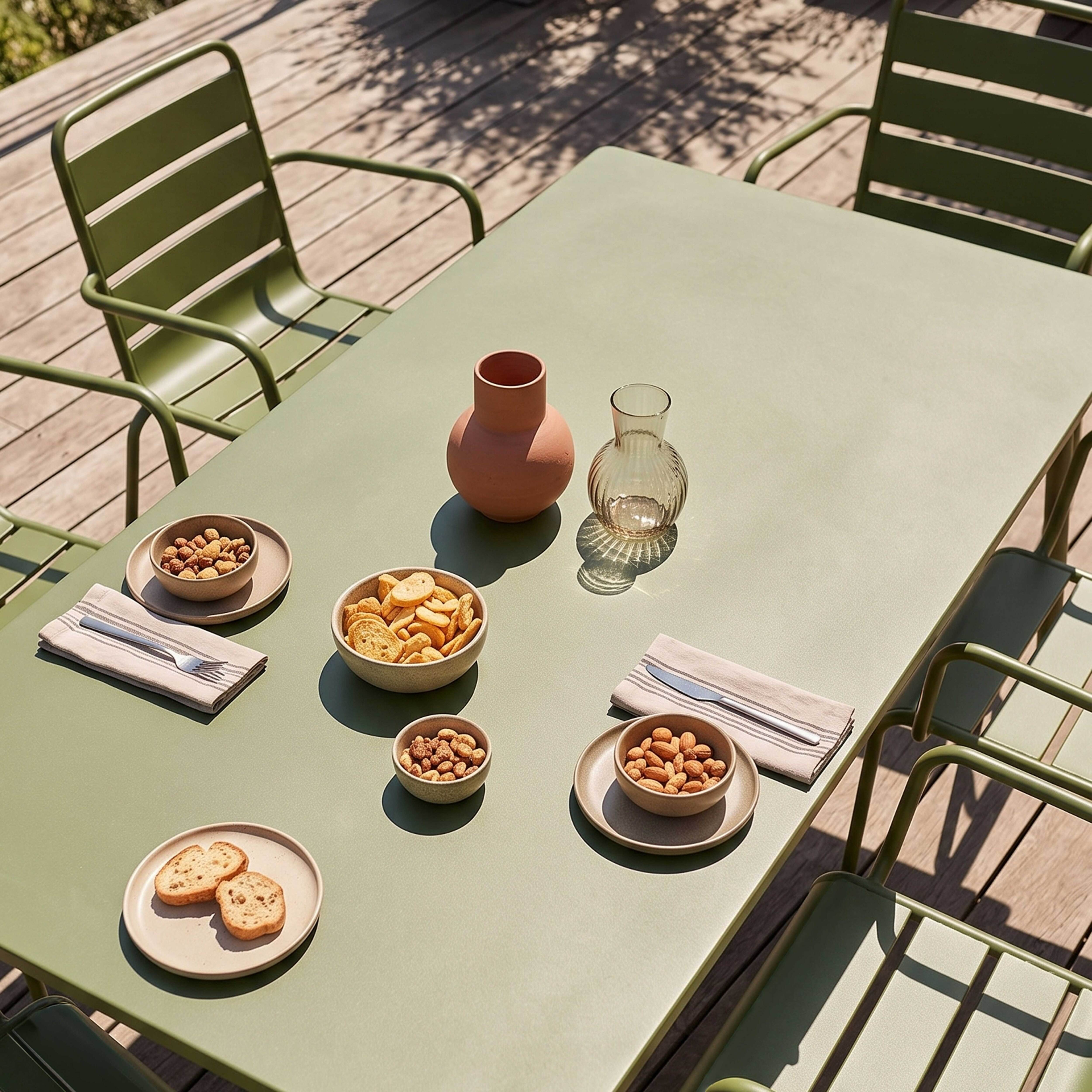 Ein Tisch im Freien mit Snacks, Vasen und grünen Stühlen.