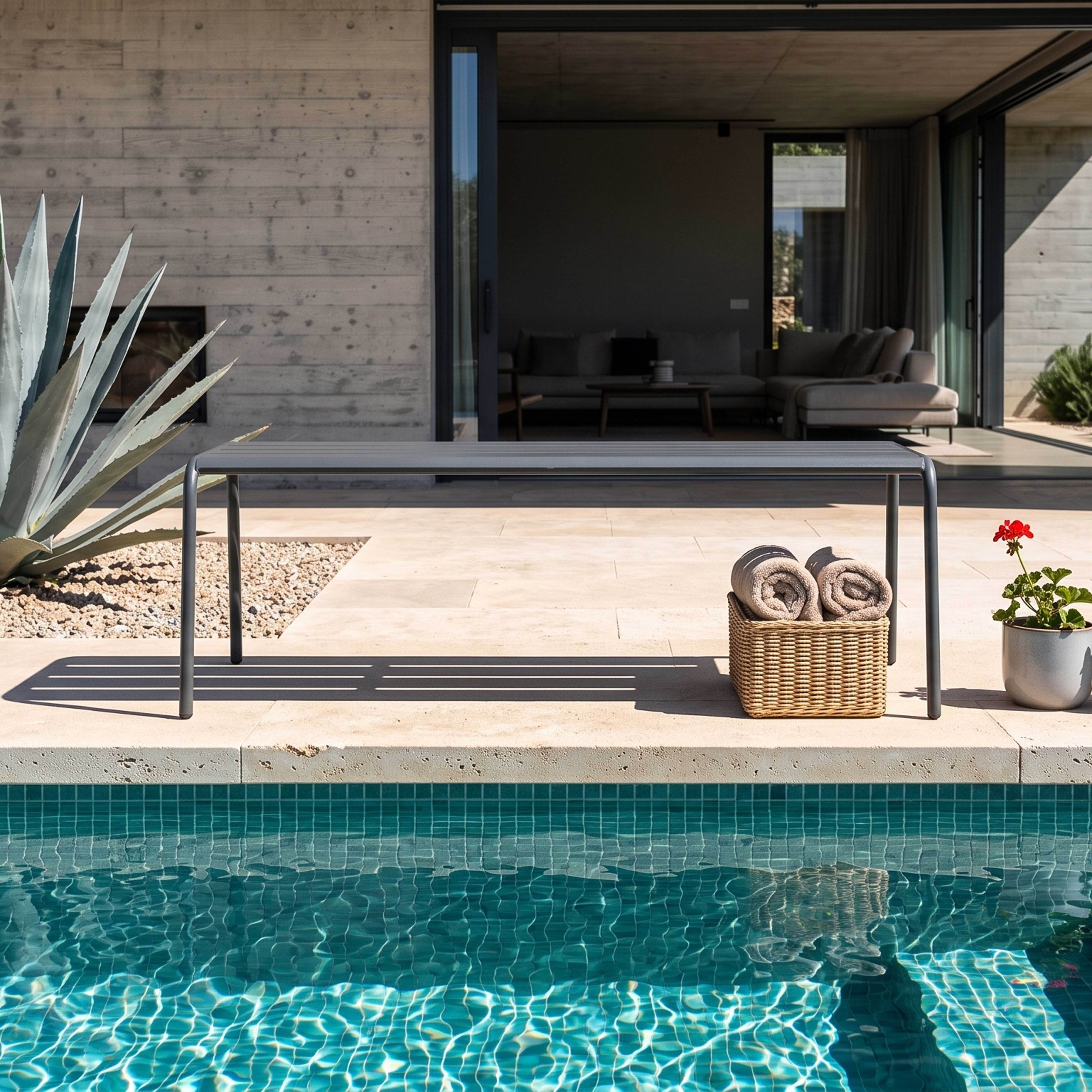 Ein moderner Tisch und ein Korb mit Handtüchern neben einem Pool.
