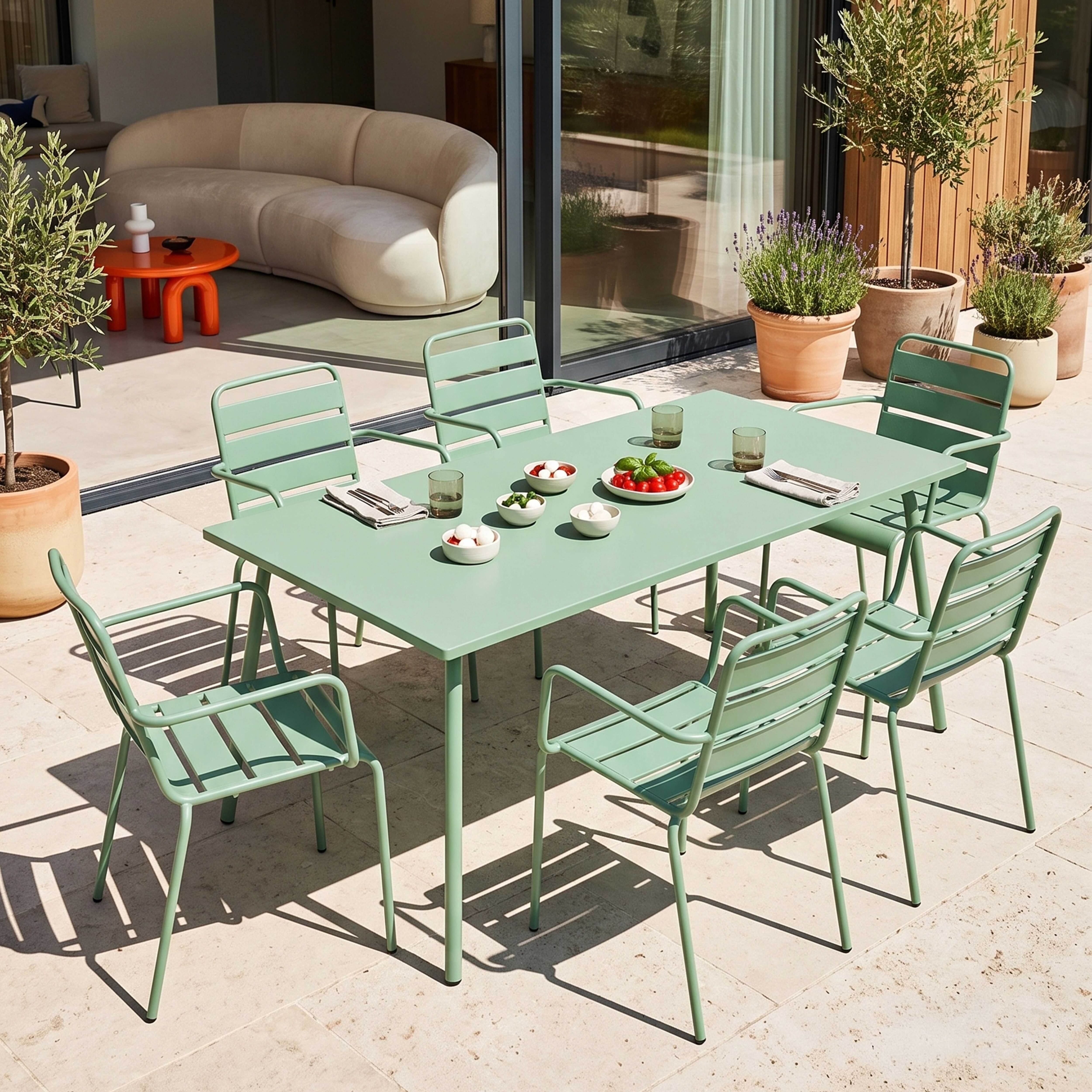 Ein hellgrüner Gartentisch mit Stühlen und Snacks auf einer Steinterrasse.