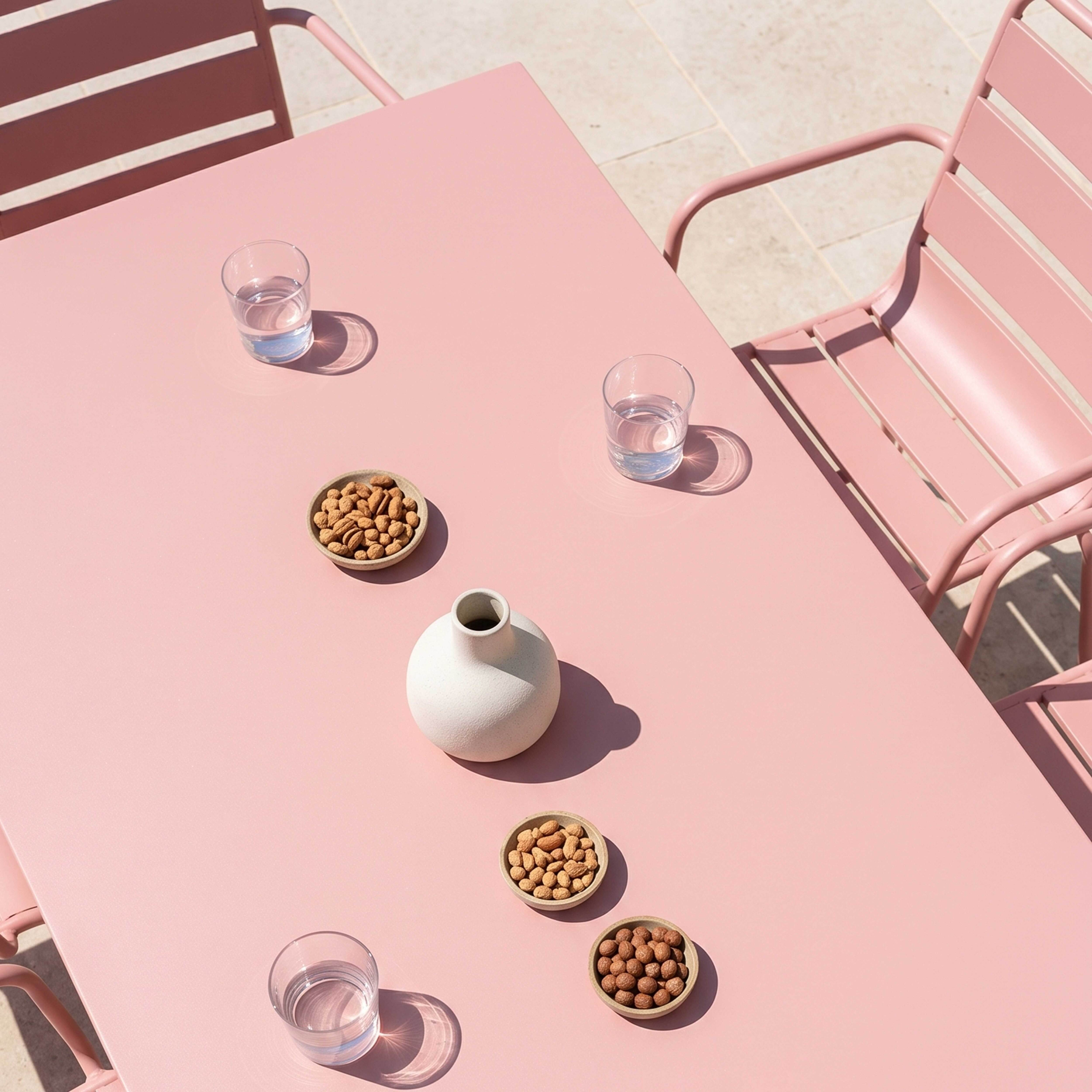 Ein rosa Tisch mit Gläsern, Vase und Nüssen, draußen.