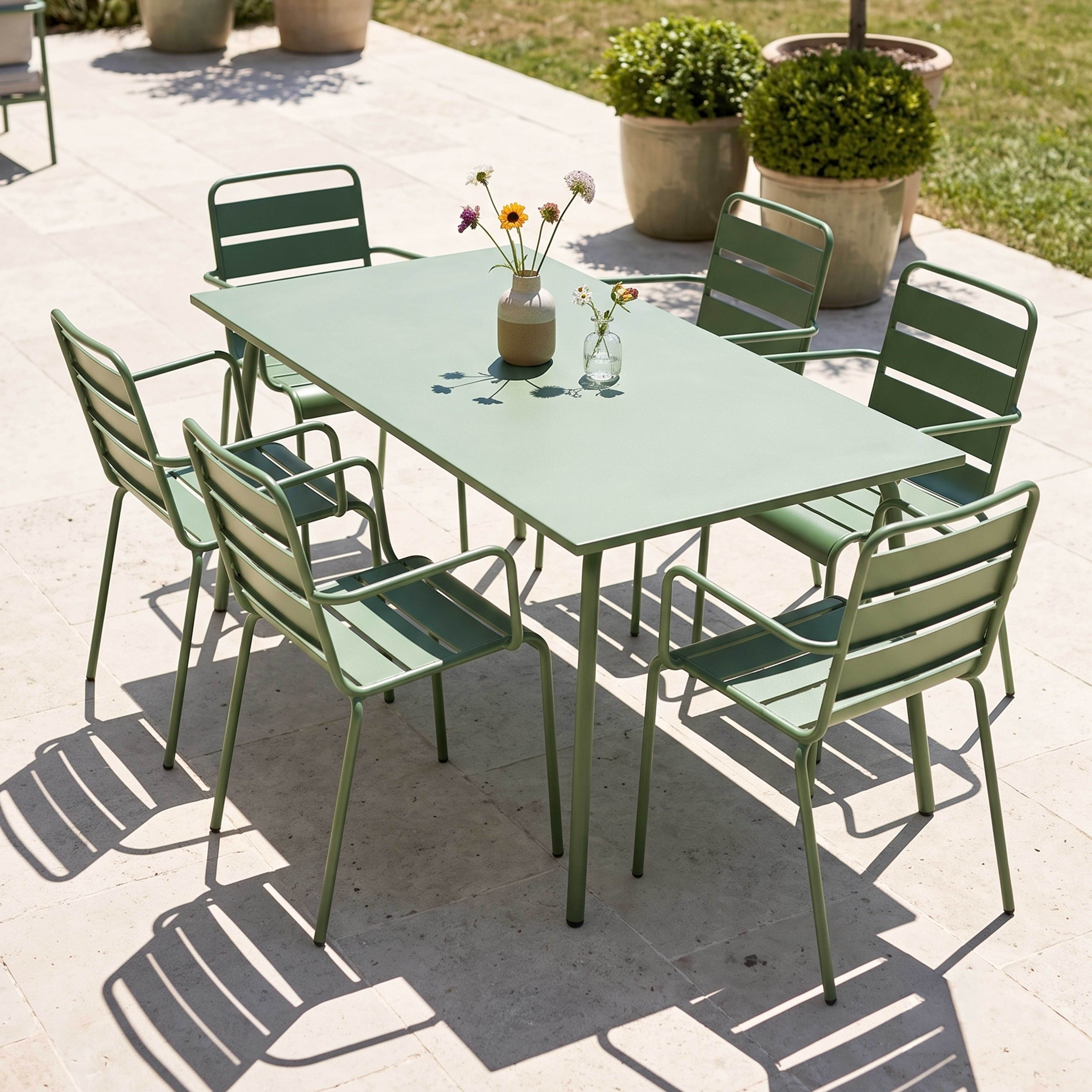 Grüner Gartentisch mit Stühlen, Blumen und Vasen im Freien.
