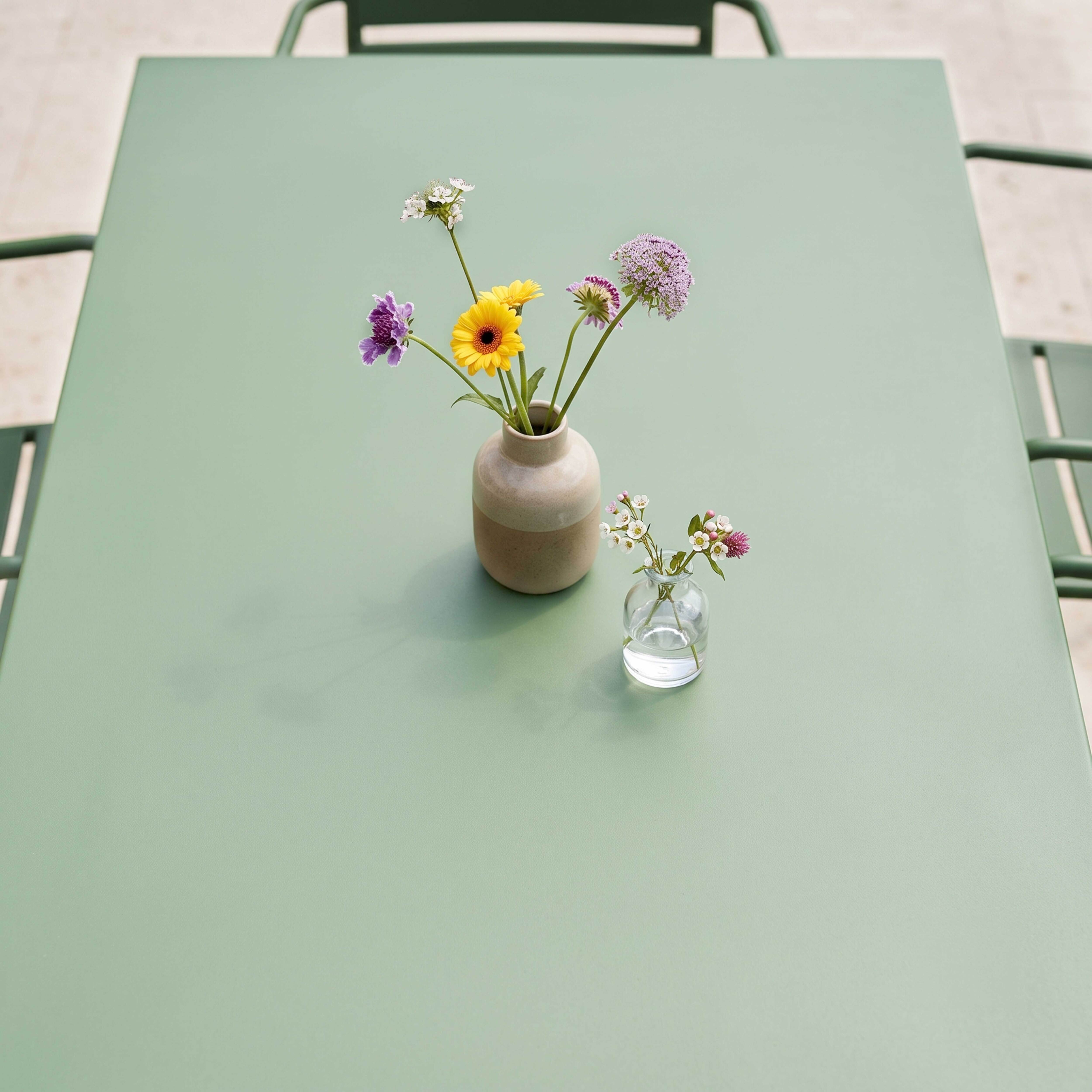 Zwei Vasen mit Blumen auf einem hellgrünen Tisch, mit Schatten.