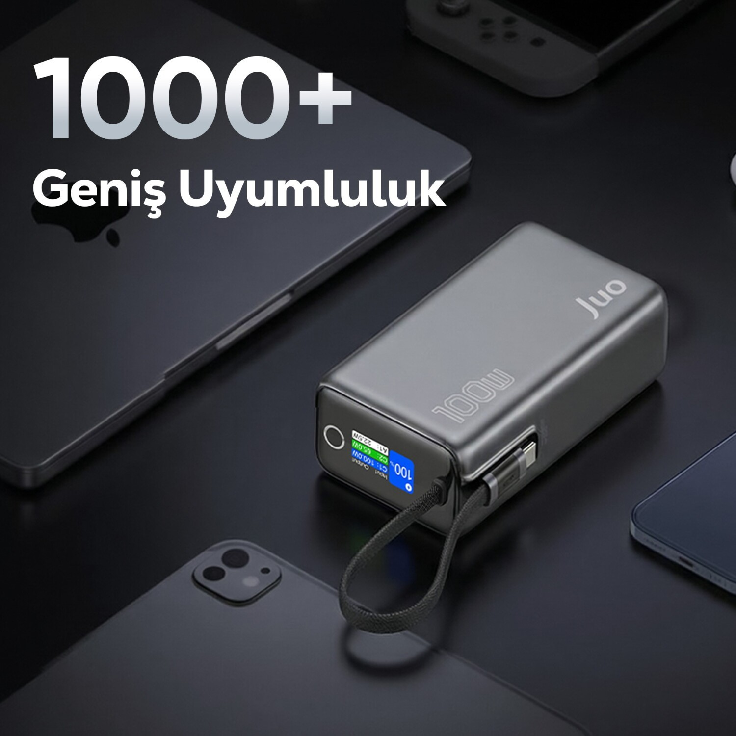 Kabloyla bağlanmış gri JUO 100W powerbank, cihazlarla çevrili.