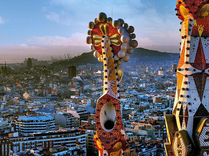 Detalle de la Sagrada Familia con la ciudad de Barcelona al fondo al atardecer.