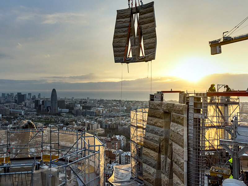 Una grúa levanta bloques de piedra sobre una ciudad al atardecer.