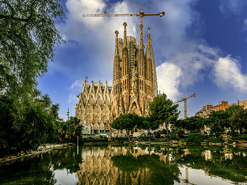 Sagrada Familia en Barcelona reflejada en un estanque, con grúas al fondo.