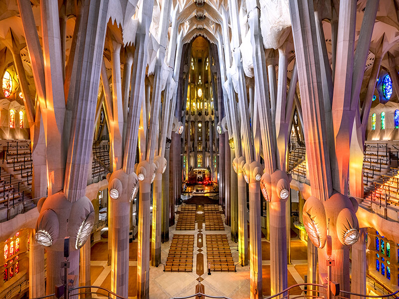 Interior de la Sagrada Familia con altas columnas y coloridos vitrales.