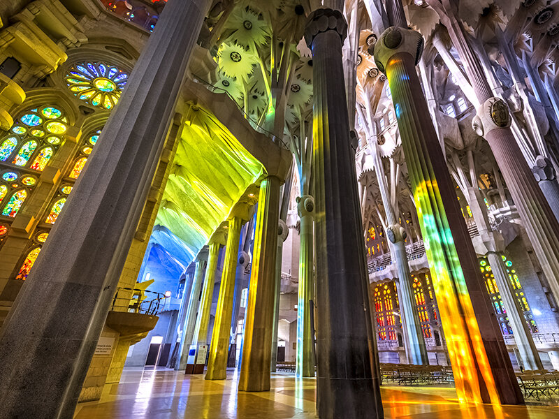 Interior de la Sagrada Familia con vidrieras coloridas que proyectan luz sobre las columnas.