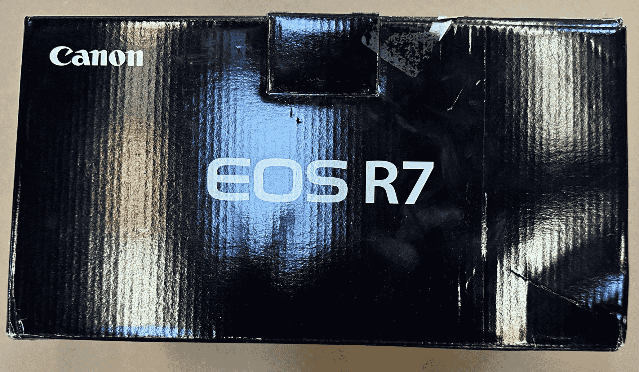 Caja negra de cámara Canon EOS R7 con crestas verticales y letras blancas.