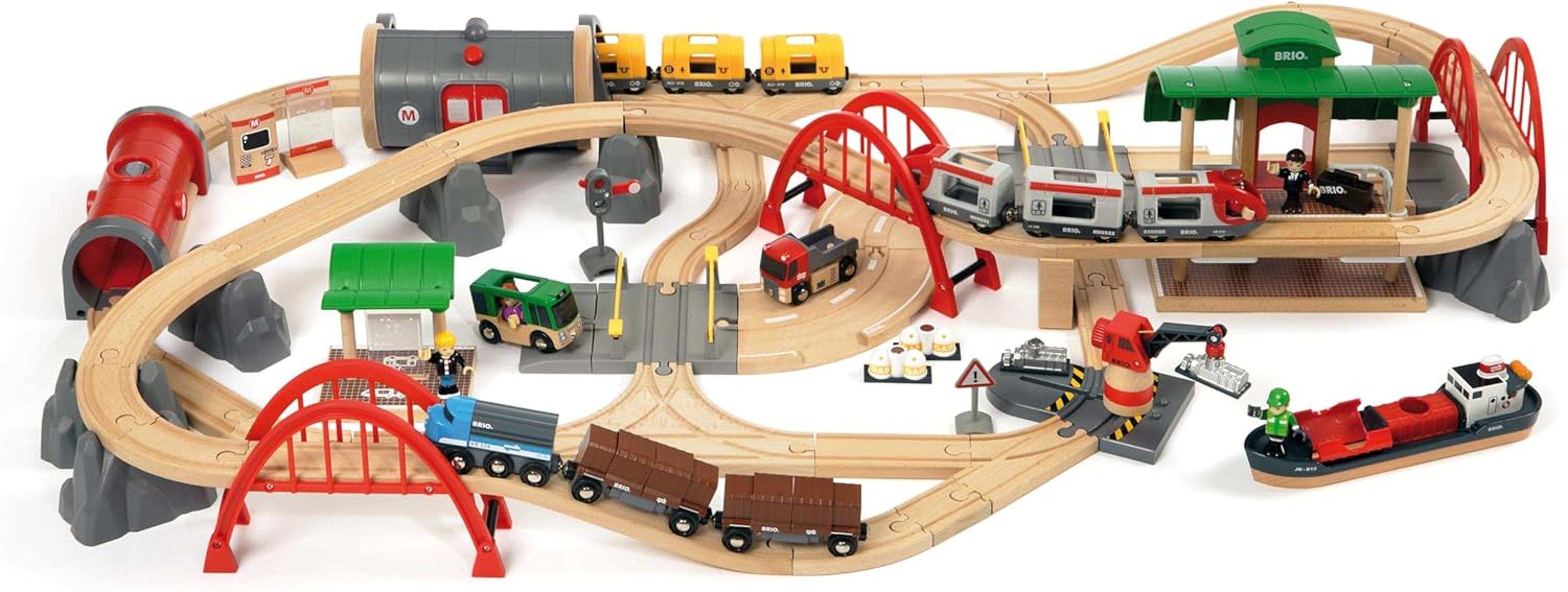 Ein hölzerner BRIO-Zugspielplatz mit Zügen, Autos, einer Station und einer Brücke.