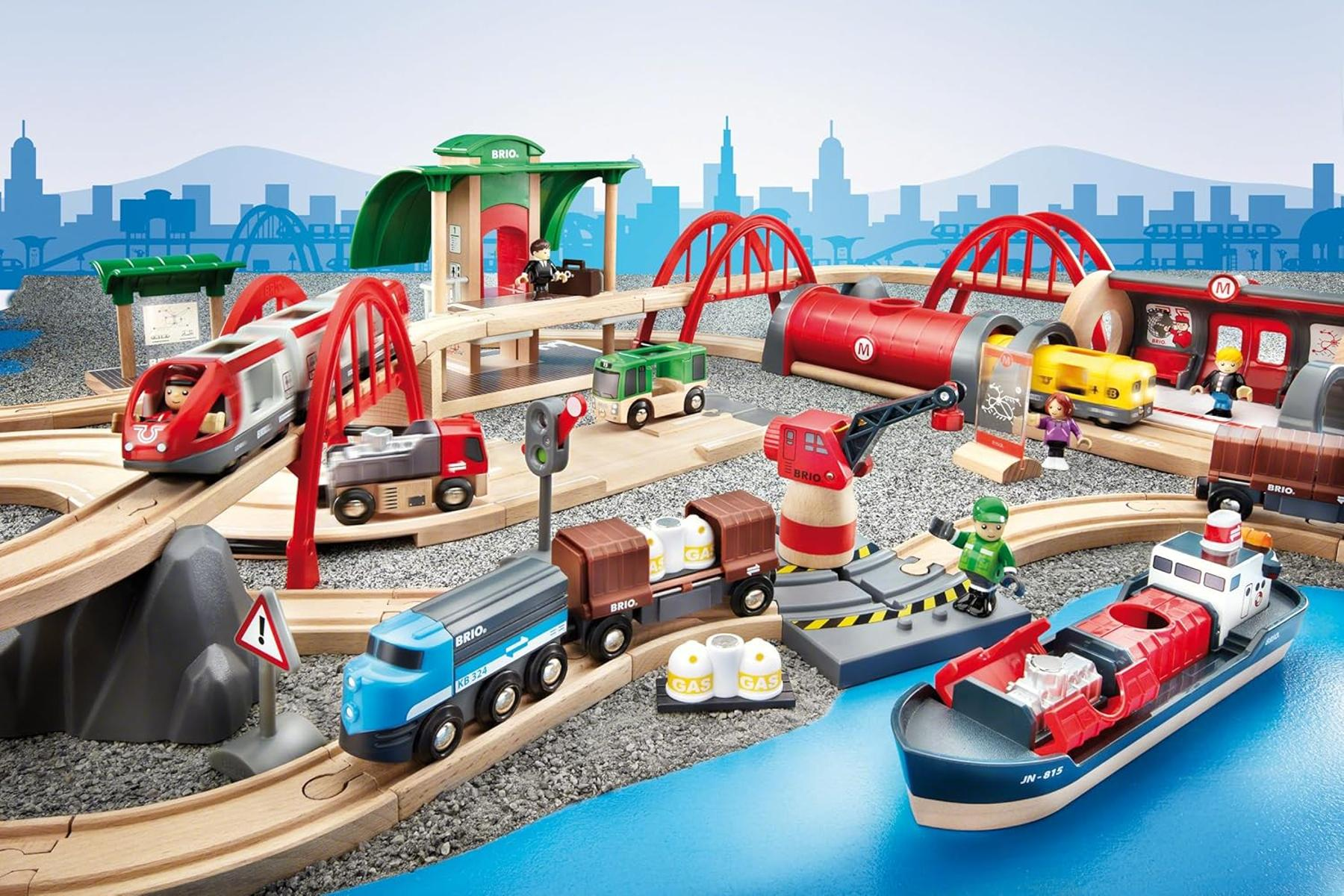 Eine Spielzeug-Eisenbahnanlage mit Zügen, Brücken, Kran, Schiff und Stadtkulisse.