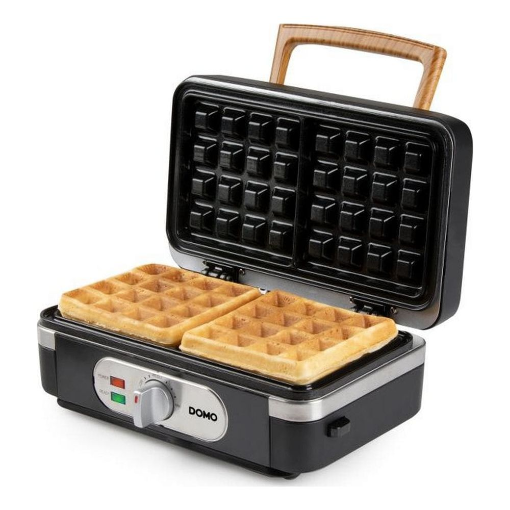 Una piastra per waffle DOMO aperta con due waffle dorati e manico in legno.