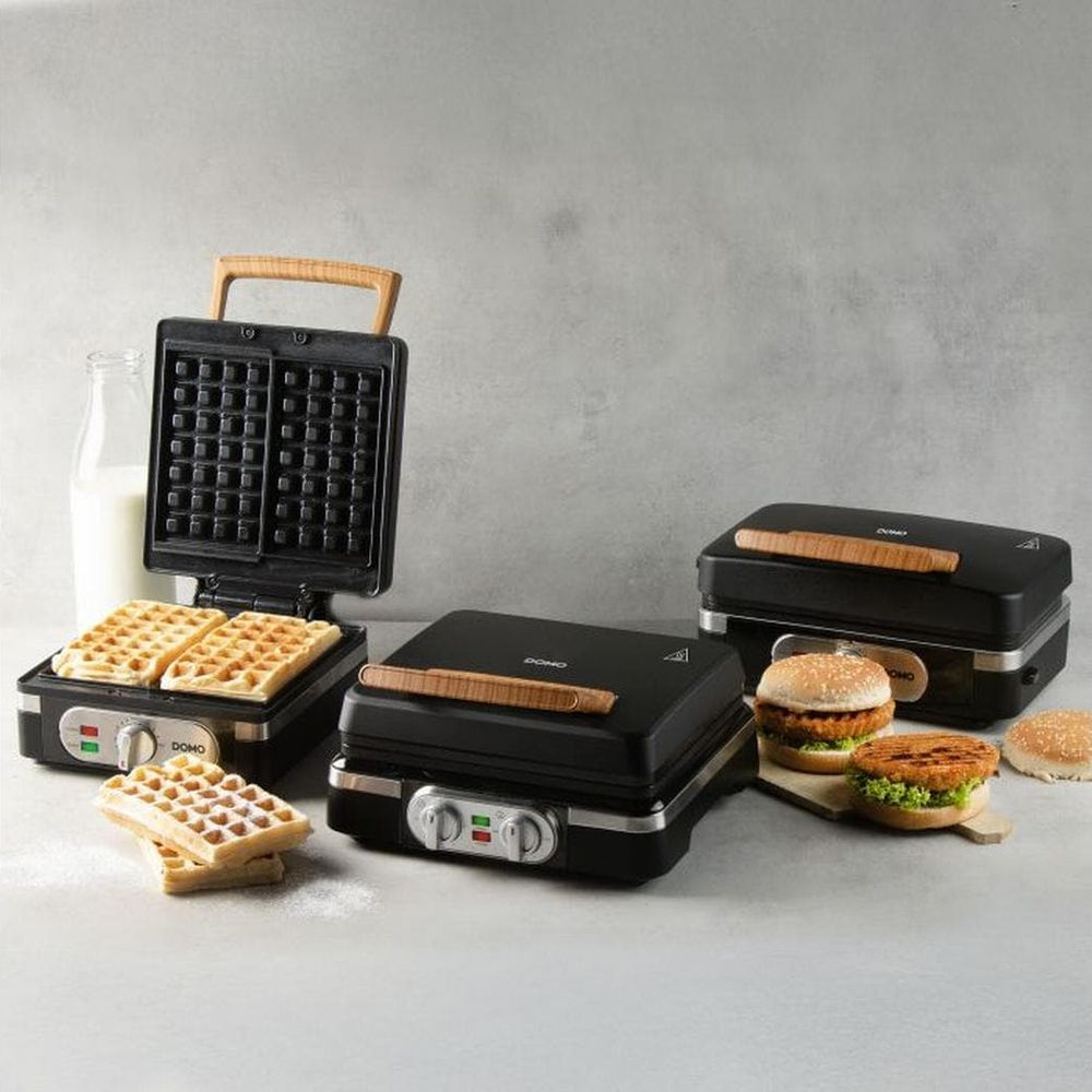 Due piastre per waffle e una sandwichiera con hamburger su un tavolo.