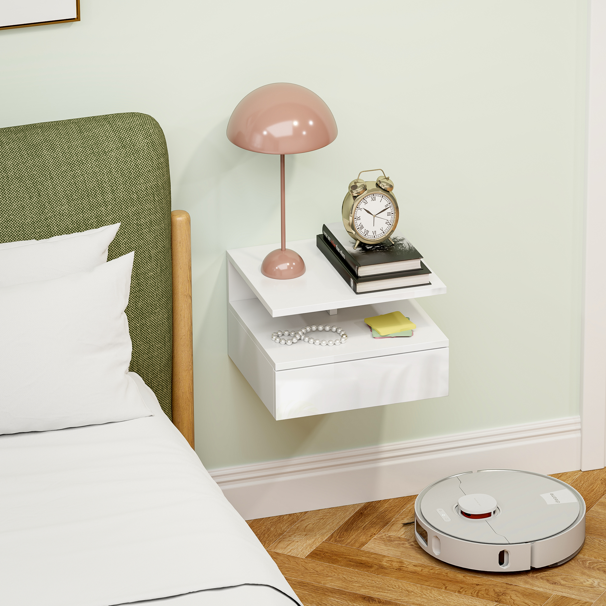 Un comodino con lampada, sveglia, libri e gioielli. Un robot aspirapolvere a terra.