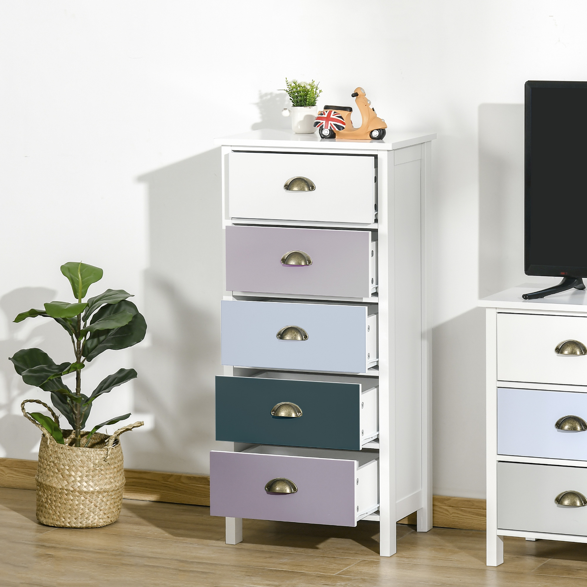Comodino bianco con cinque cassetti color pastello, accanto a un TV e una pianta.